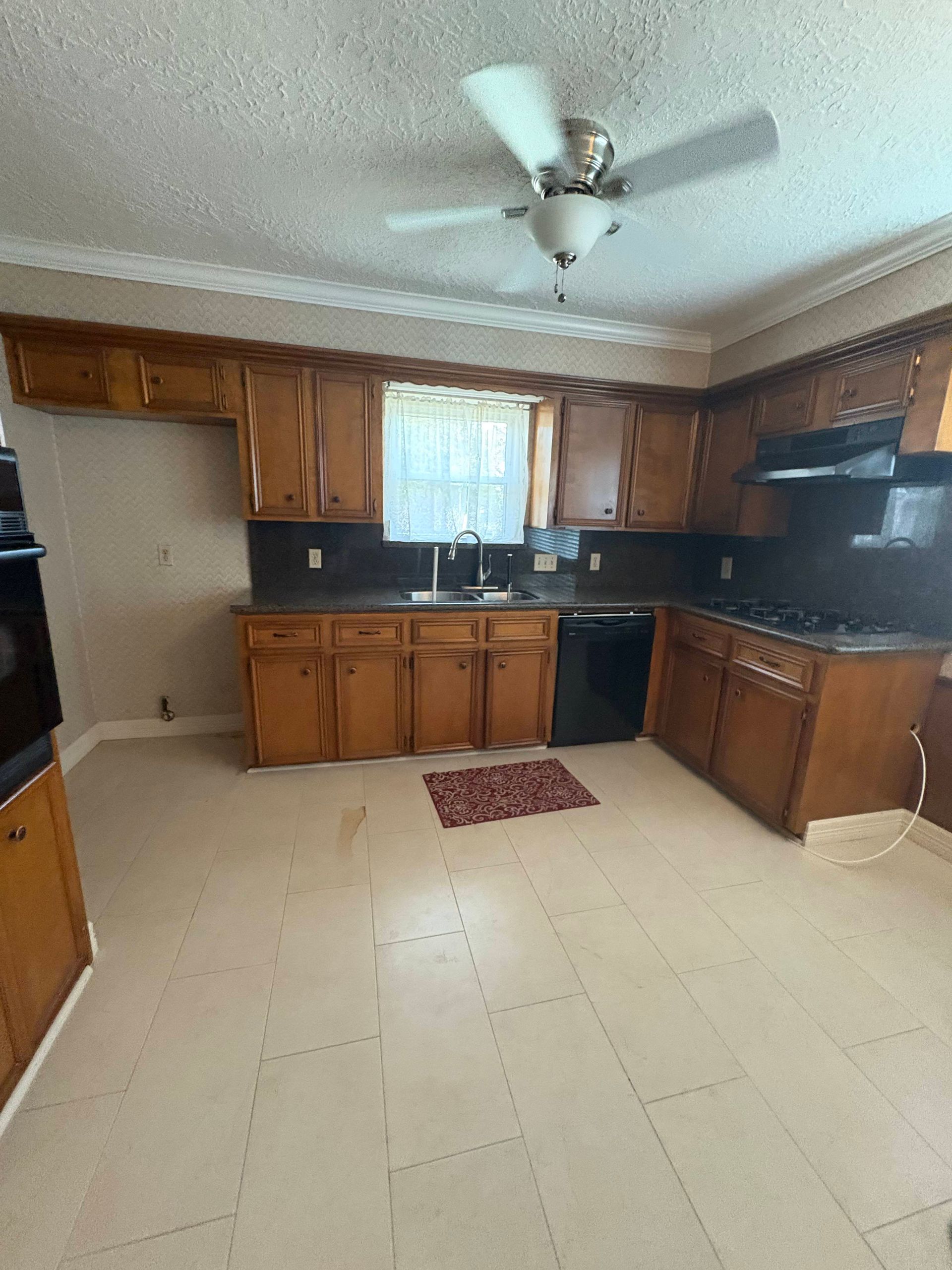 Kitchen with wooden cabinets, black appliances, and tan floor tiles. A ceiling fan is present.