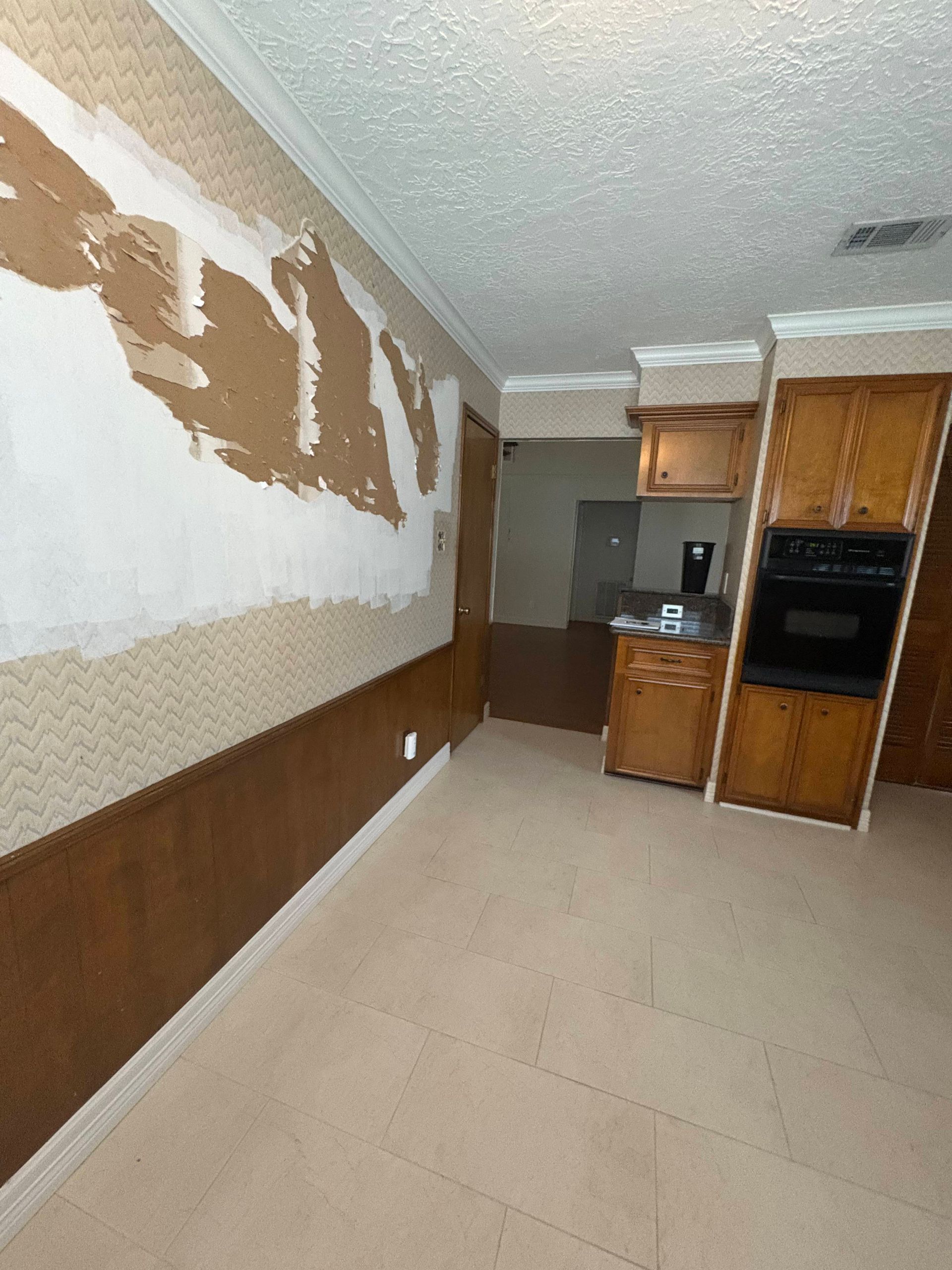 Wall with exposed drywall, wood paneling, kitchen cabinets, and oven.