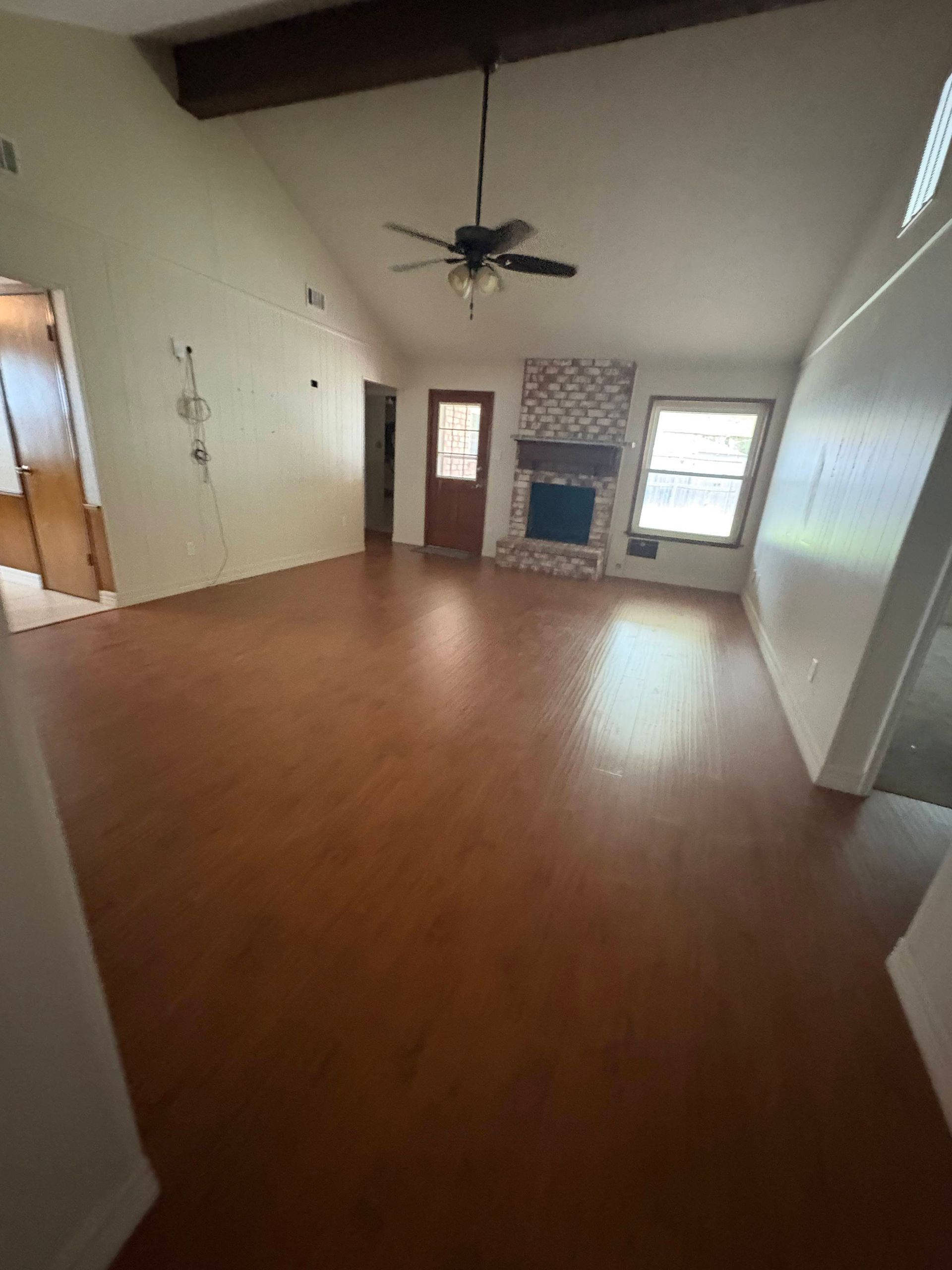 Spacious living room with wood floor, fireplace, and high ceiling with dark wood beam.