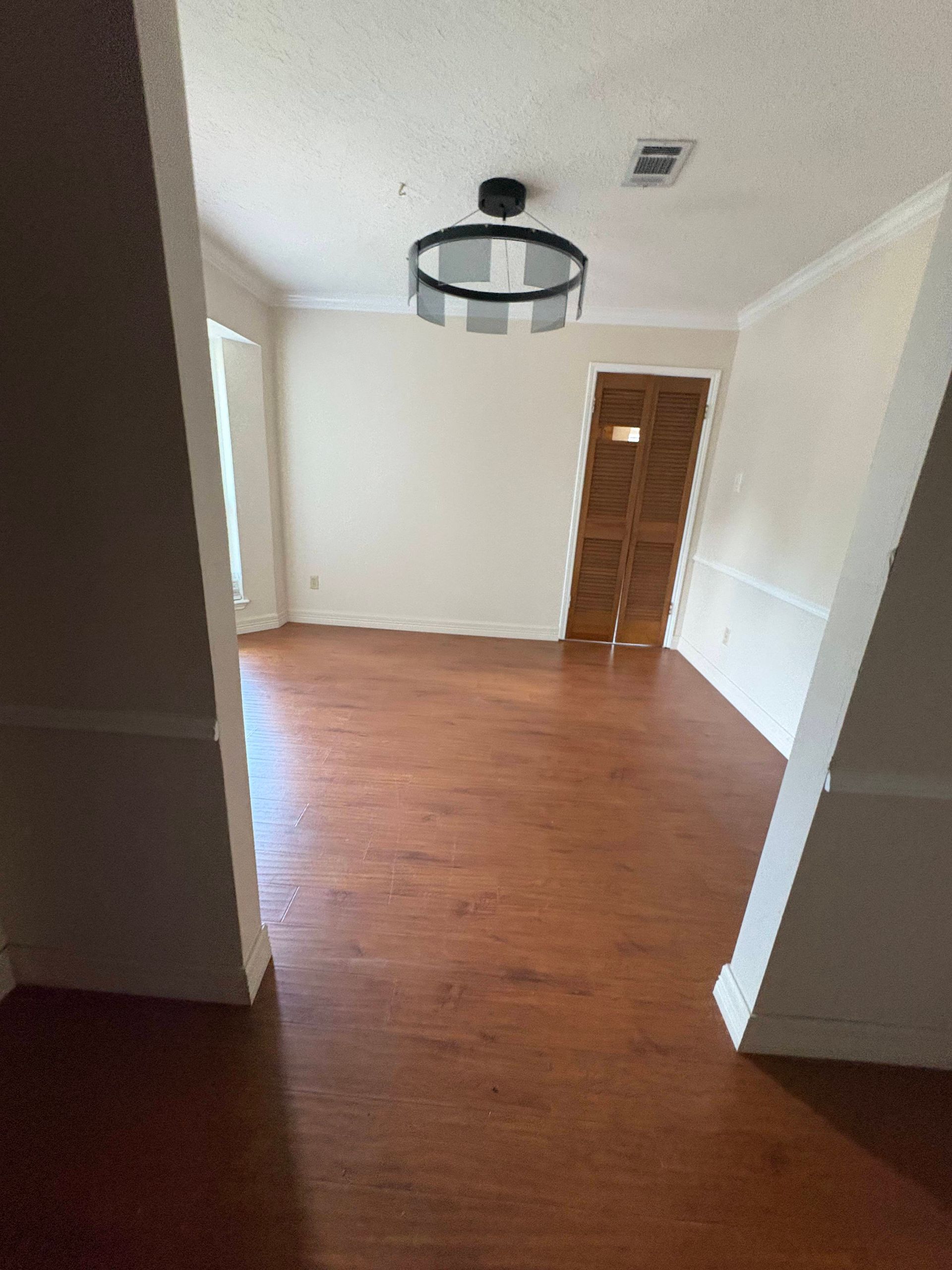 Empty room with brown wooden floors, white walls, and a circular light fixture. A wooden door is at the back.