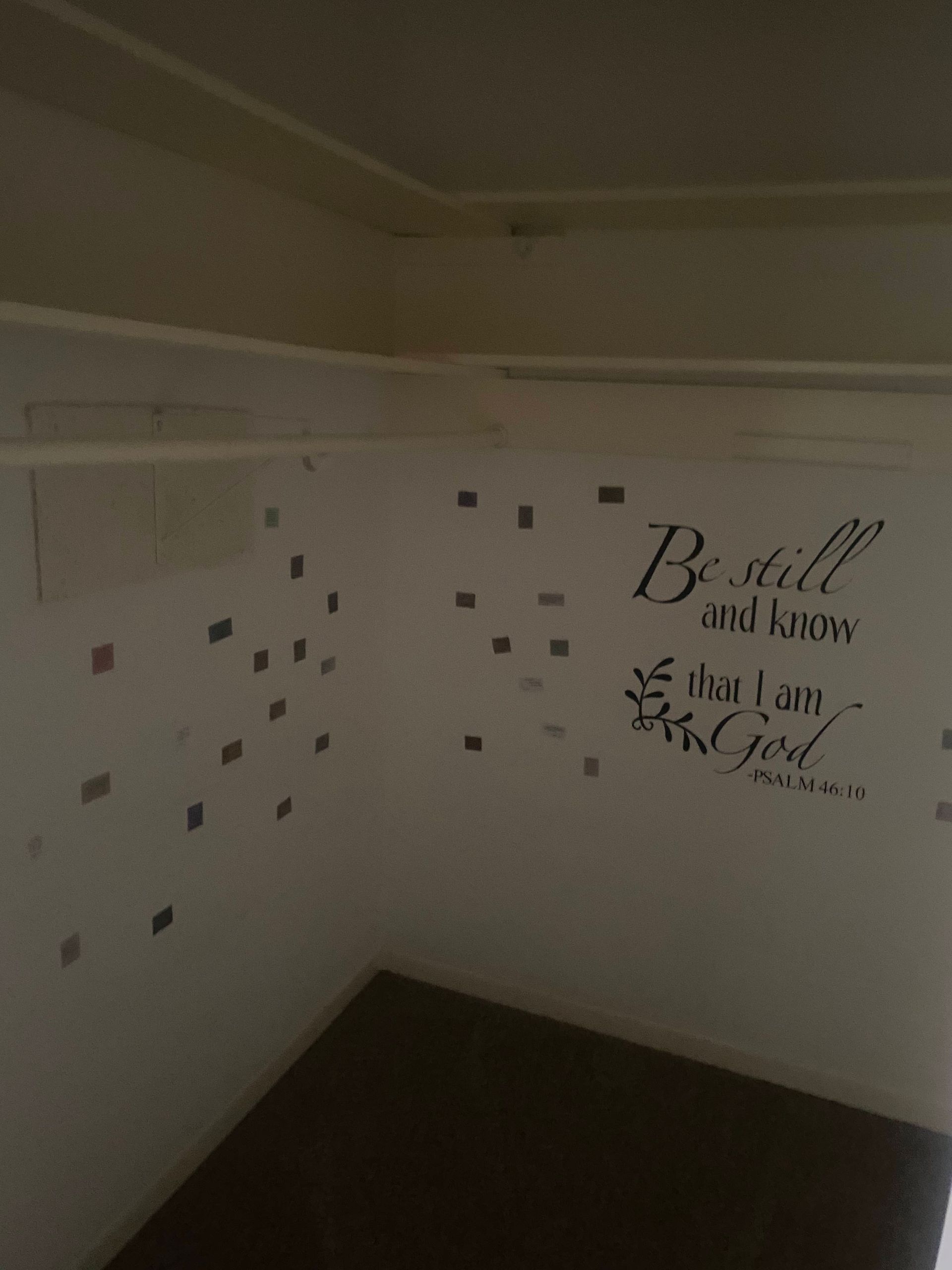 Corner of a white wall with a scripture decal and scattered square stickers. A dark surface is below.