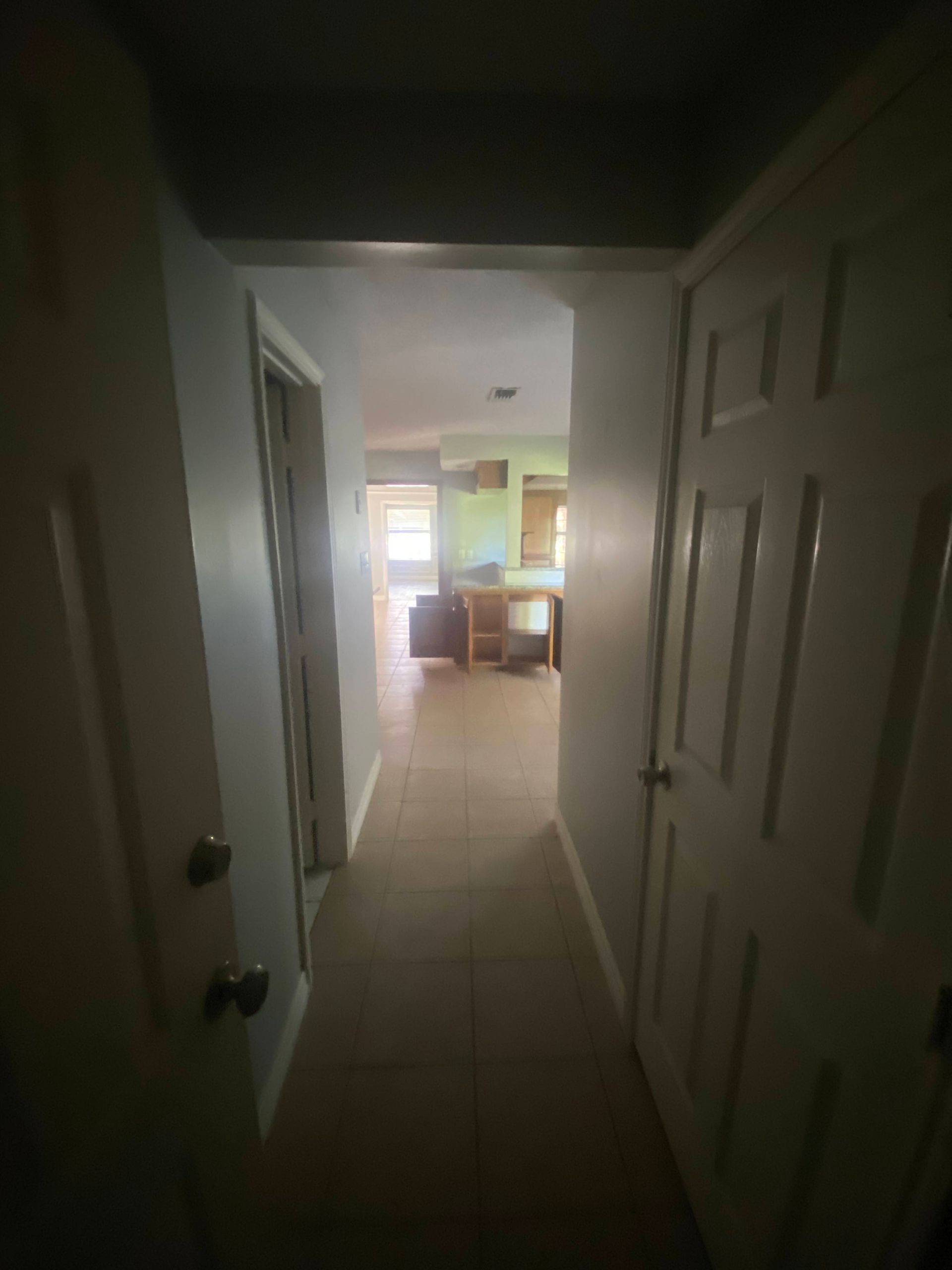 Narrow hallway leading to a room, with doors and tiled floor.