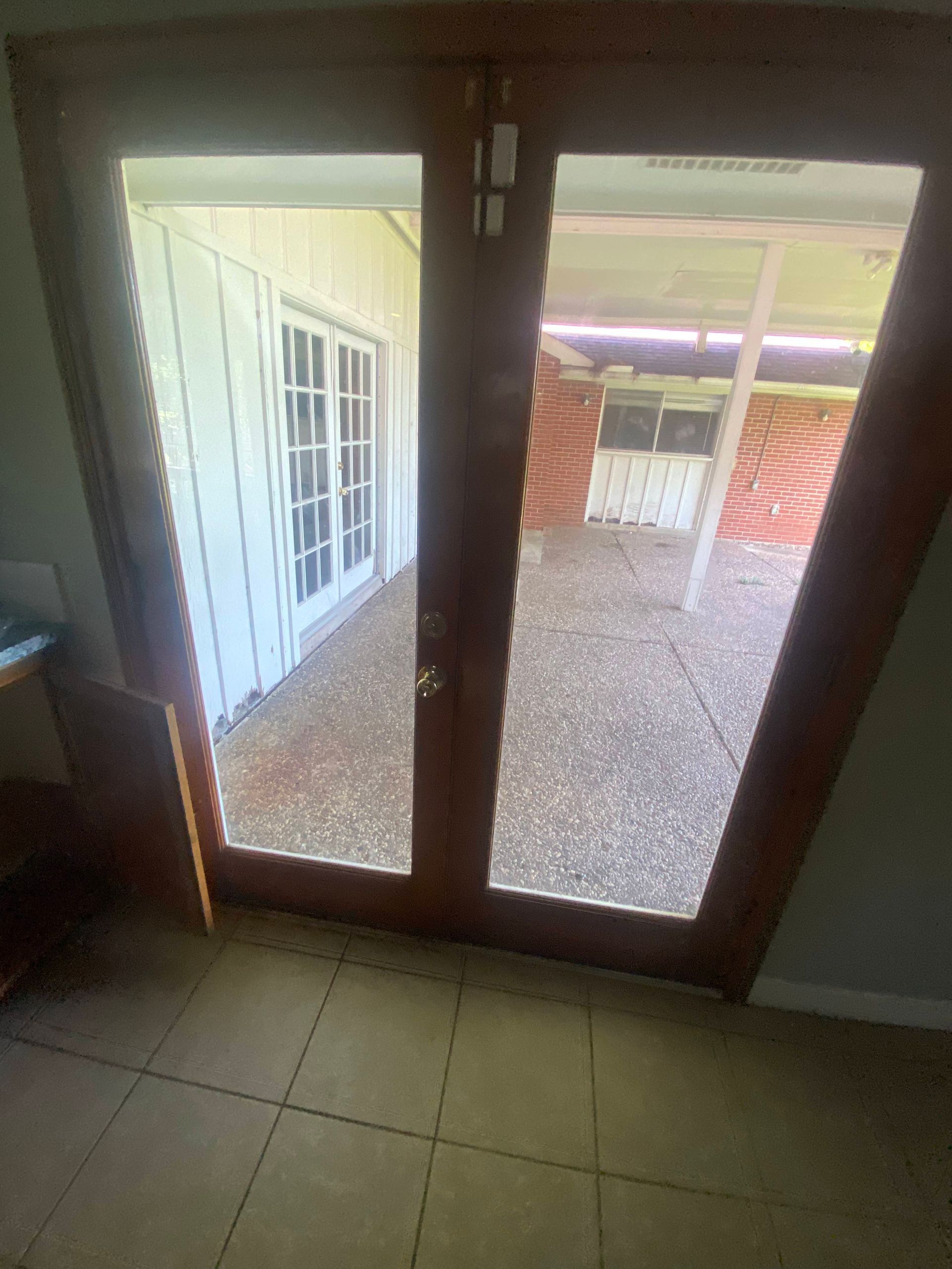 Wooden French doors open onto a concrete patio. The interior shows a tiled floor.