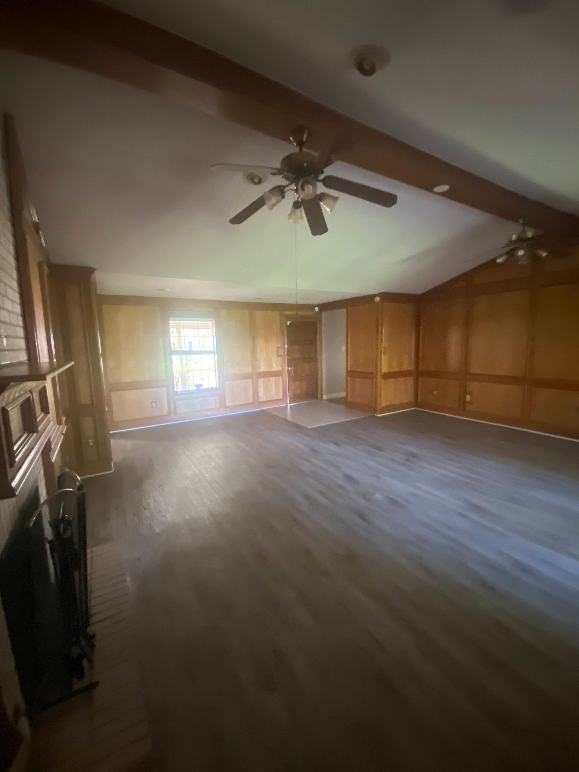 Empty living room with wood paneling, a fireplace, and a ceiling fan.