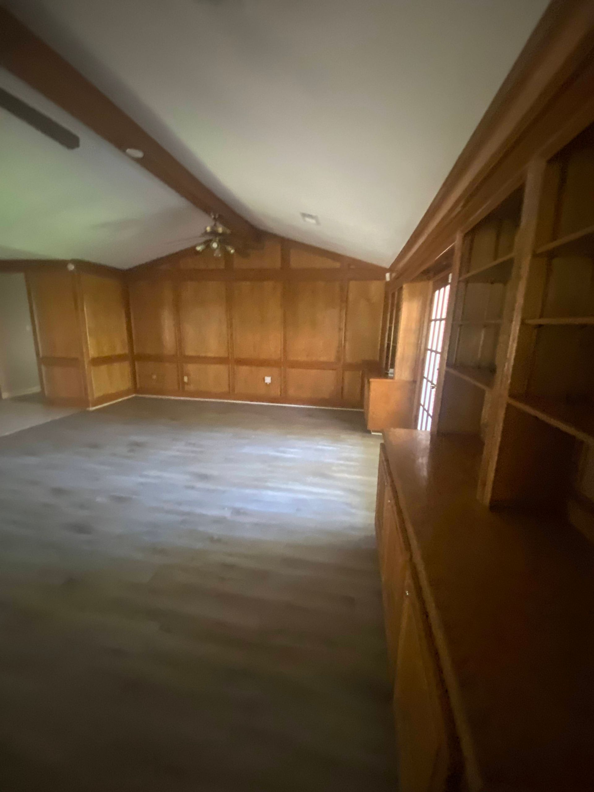 Empty living room with wood paneling, built-in shelves, and a sloped ceiling.