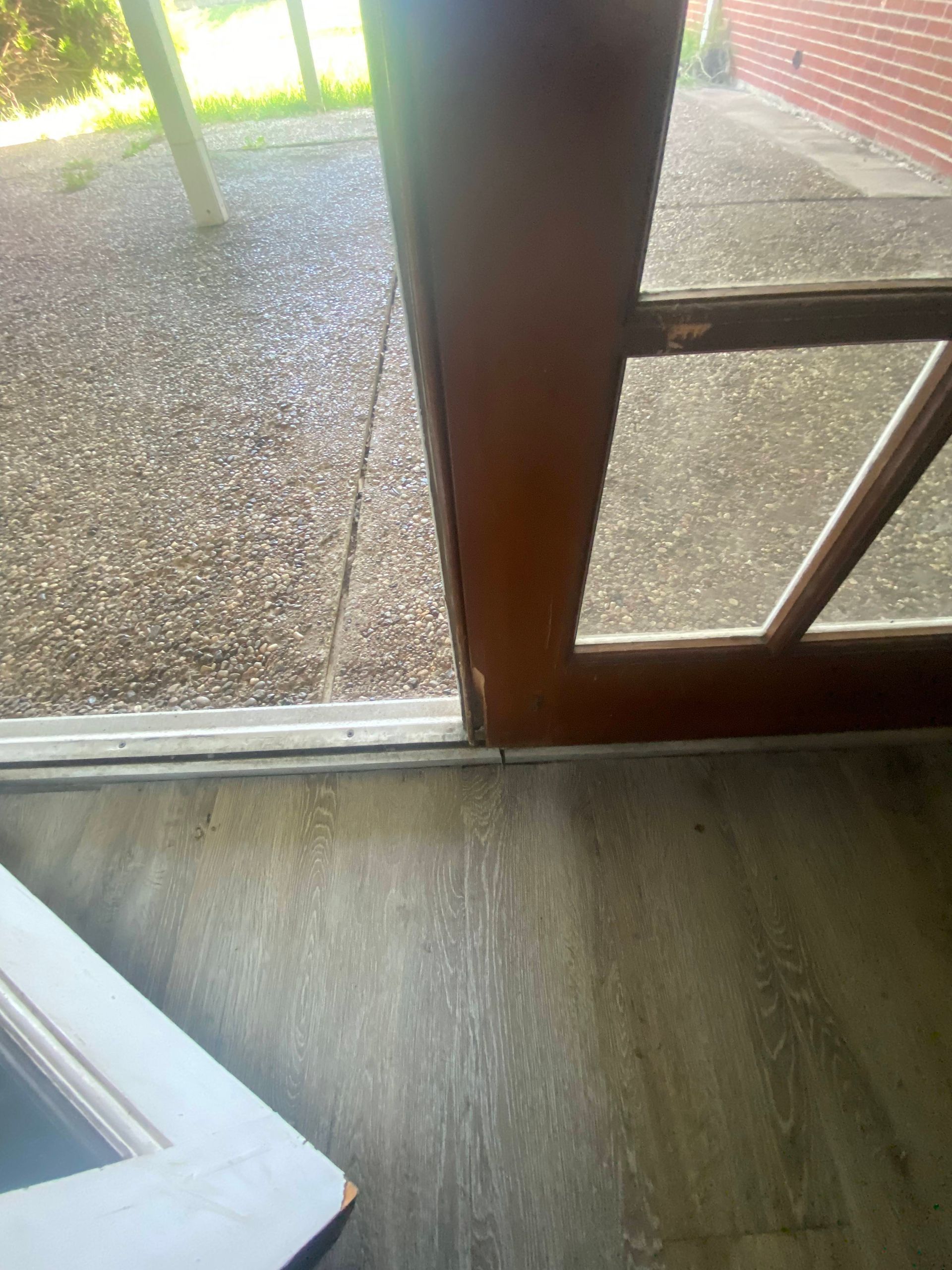 Door, close-up, wood frame, glass pane, threshold. Sunlight on porch, interior flooring.