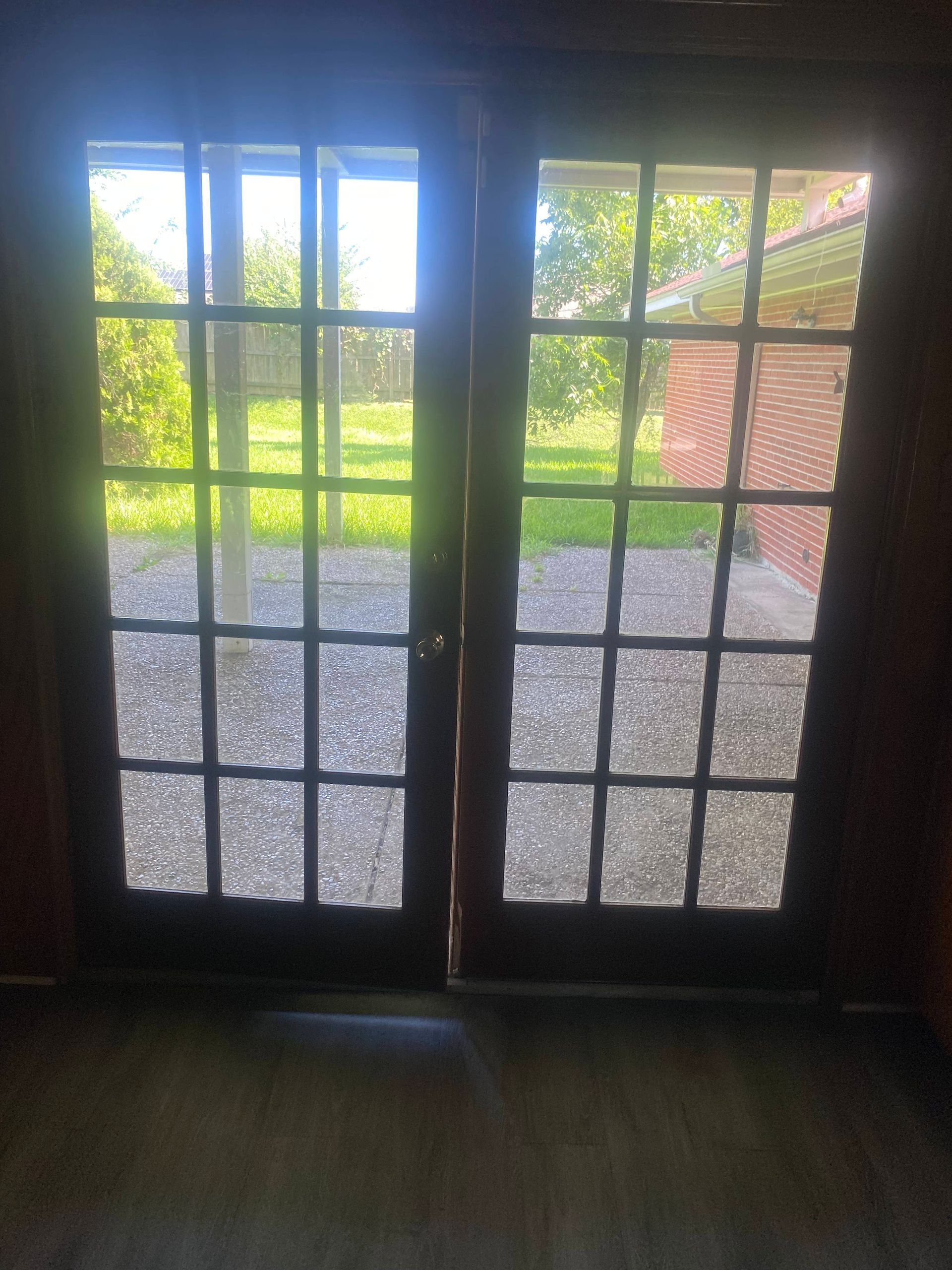 French doors with multiple window panes, leading to a yard with grass and a brick building.