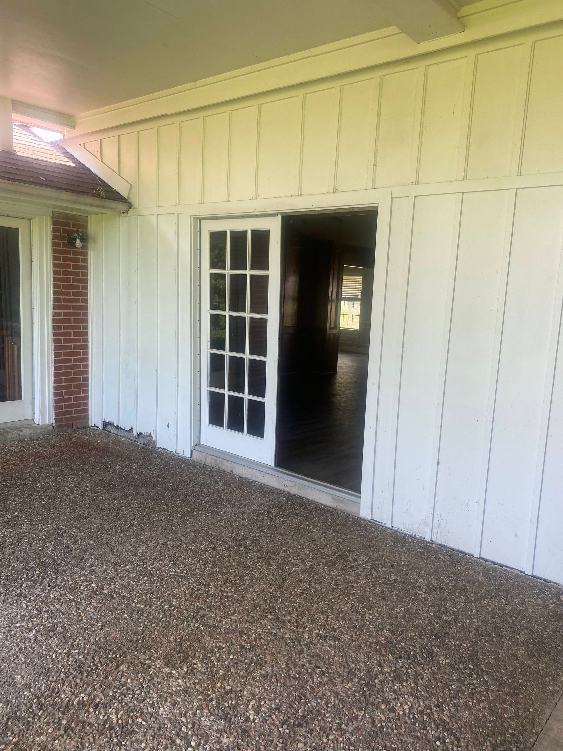 White door opens to a home interior. Gravel-covered porch beneath a white-paneled roof.