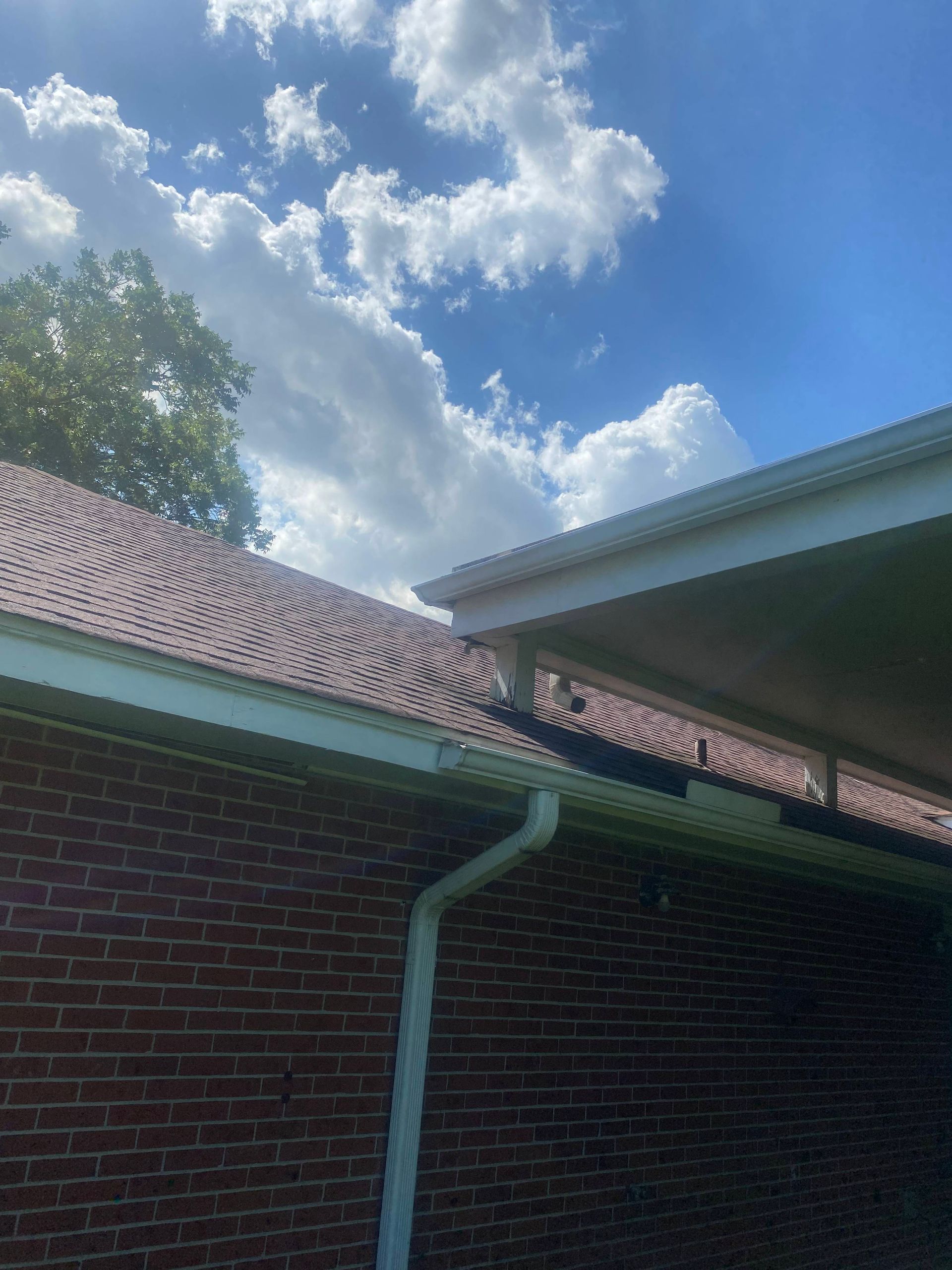Brick building with a brown shingled roof, white gutters, and blue sky with clouds.
