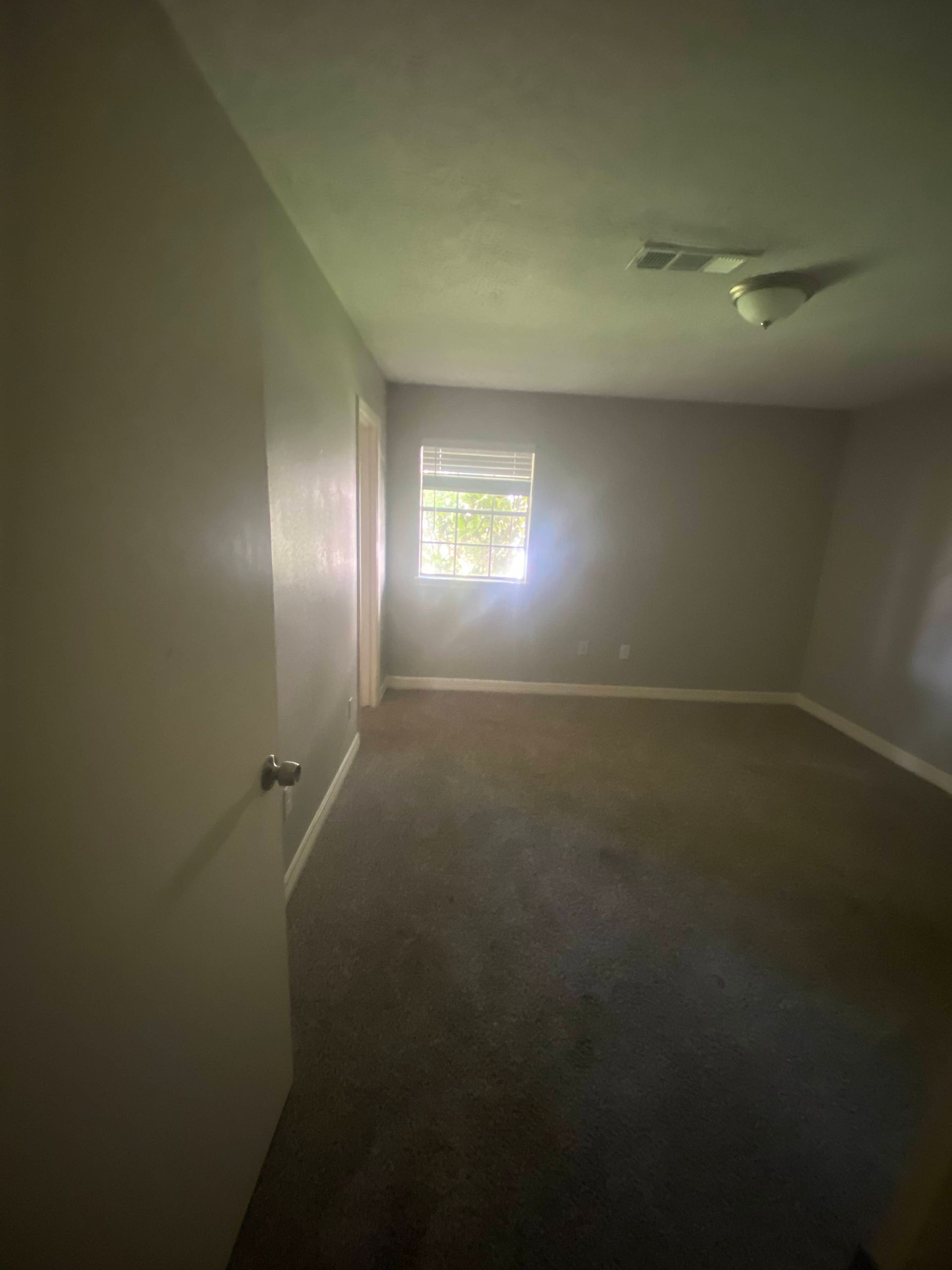 Empty room with grey carpet, small window, and light colored walls.