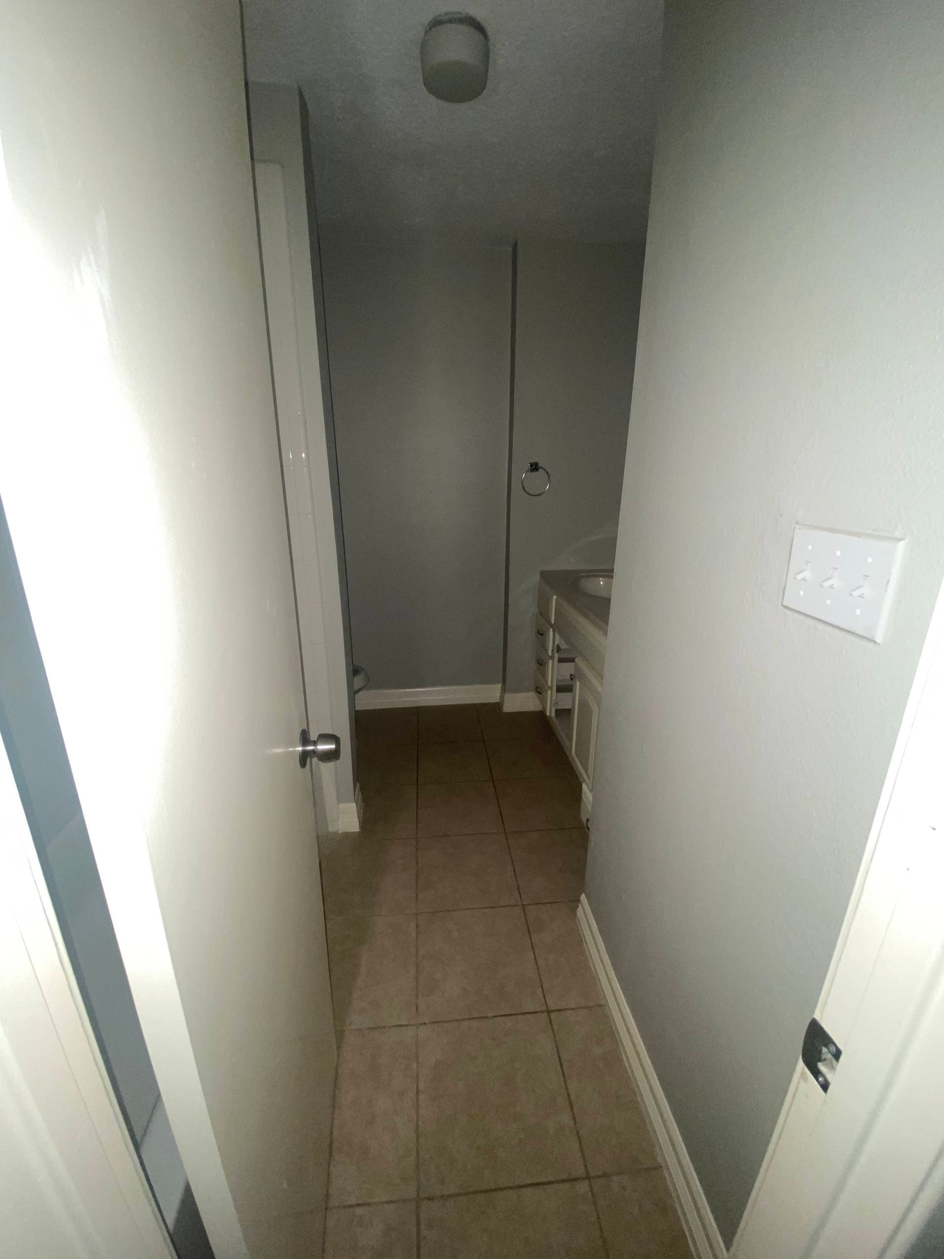 Narrow hallway with gray walls, tiled floor, and a light fixture on the ceiling.