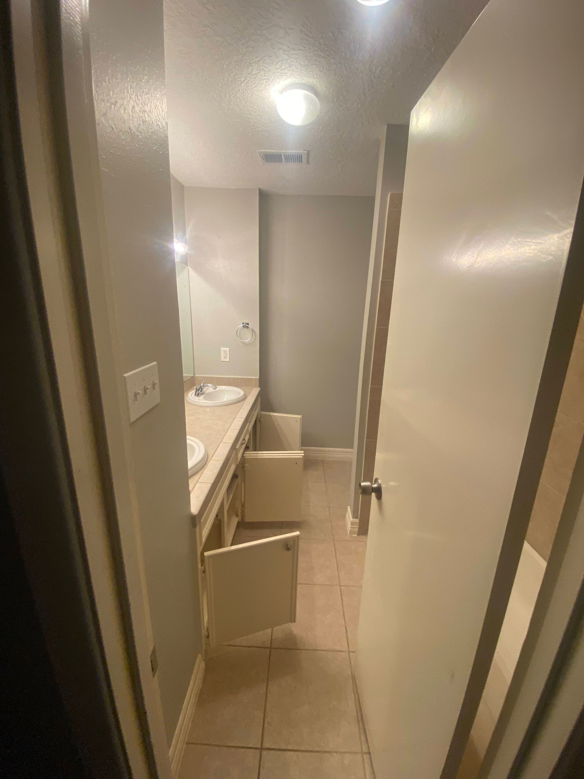 Bathroom hallway with open cabinet doors and a vanity. Beige tile floor and gray walls.