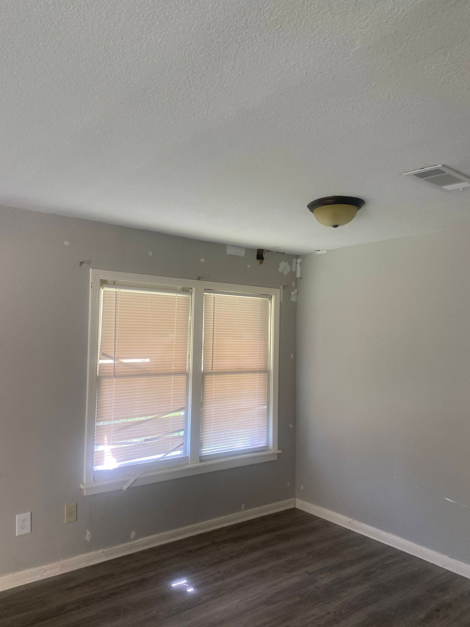 Room interior with window, blinds, and peeling paint on the ceiling. Hardwood floor and a light fixture.