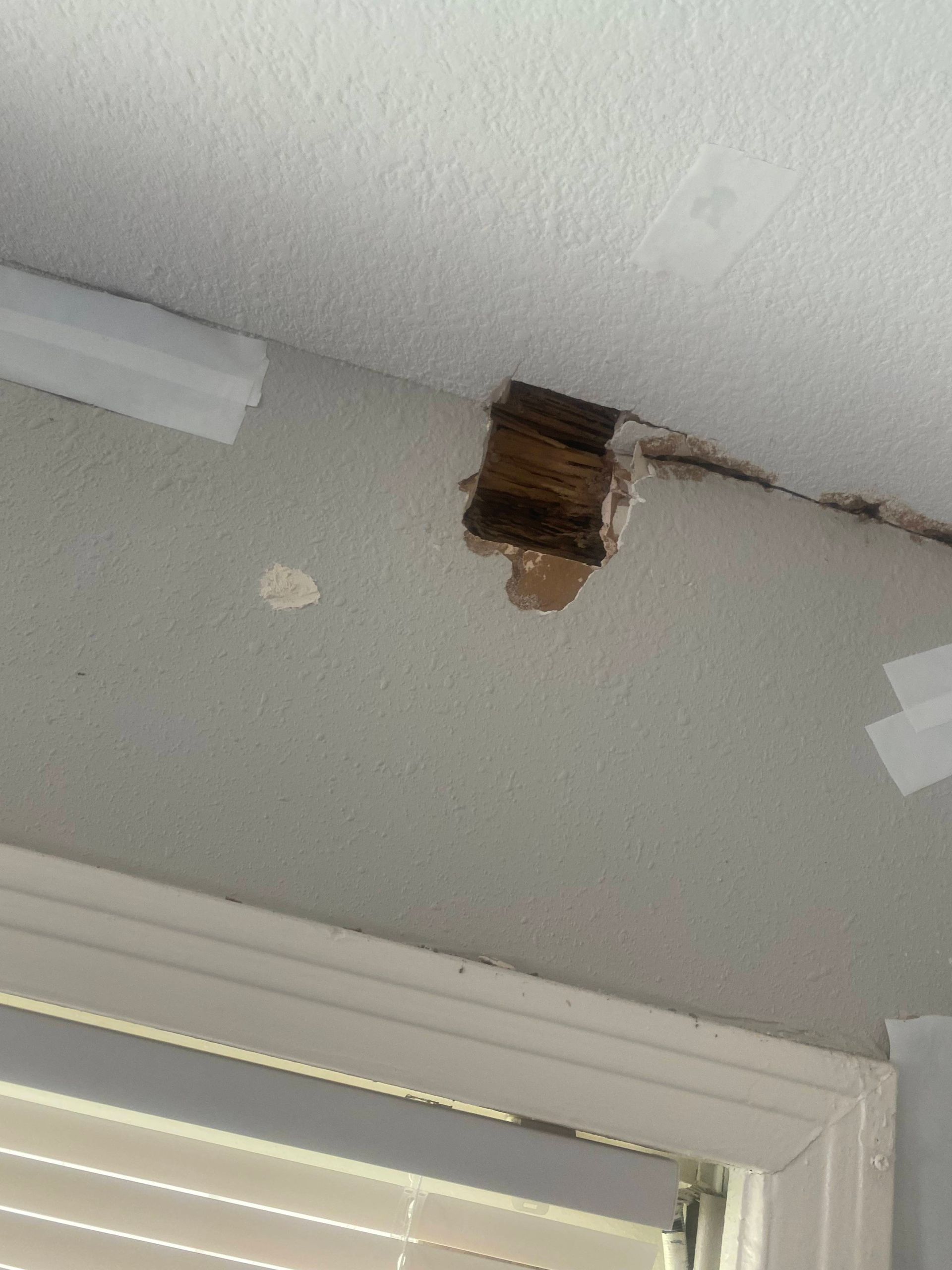 Hole in wall near ceiling, revealing wood framing. White ceiling, gray wall, and white trim are visible.