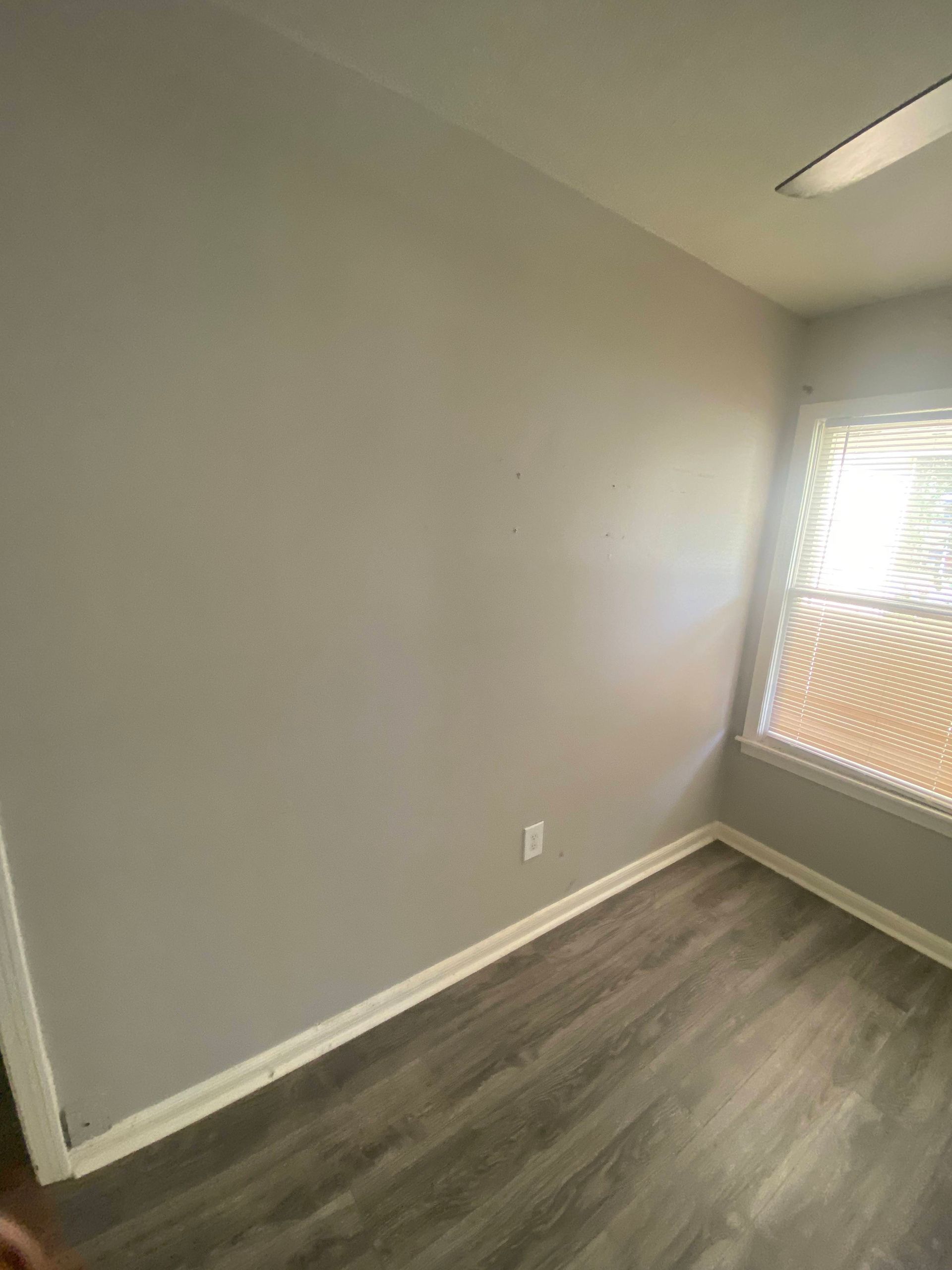 Empty room with gray walls, wood-look flooring, and a window with blinds.
