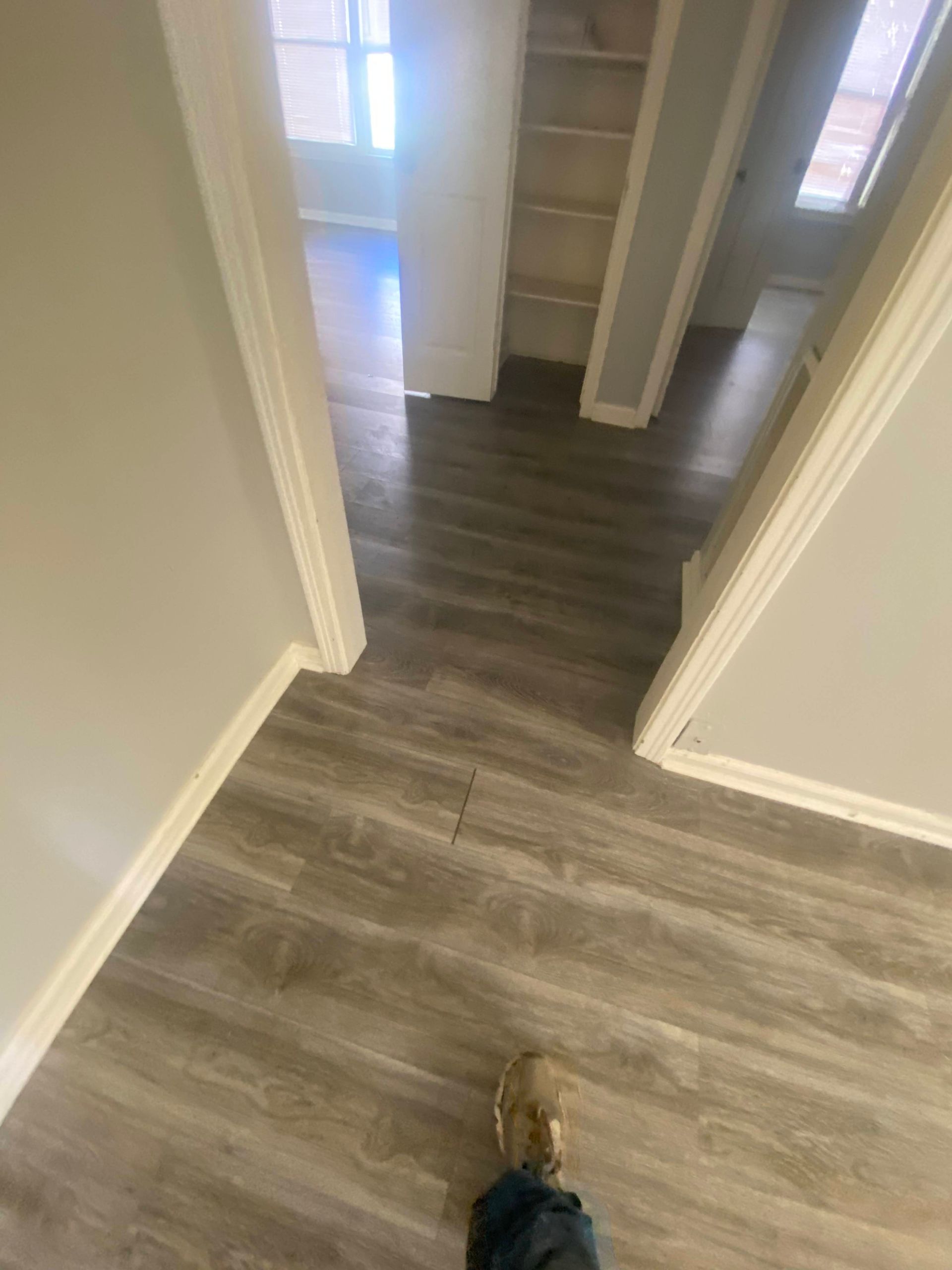 Overhead shot of a hallway with gray wood-look flooring. Visible doorways, walls are light gray, and trim is white.