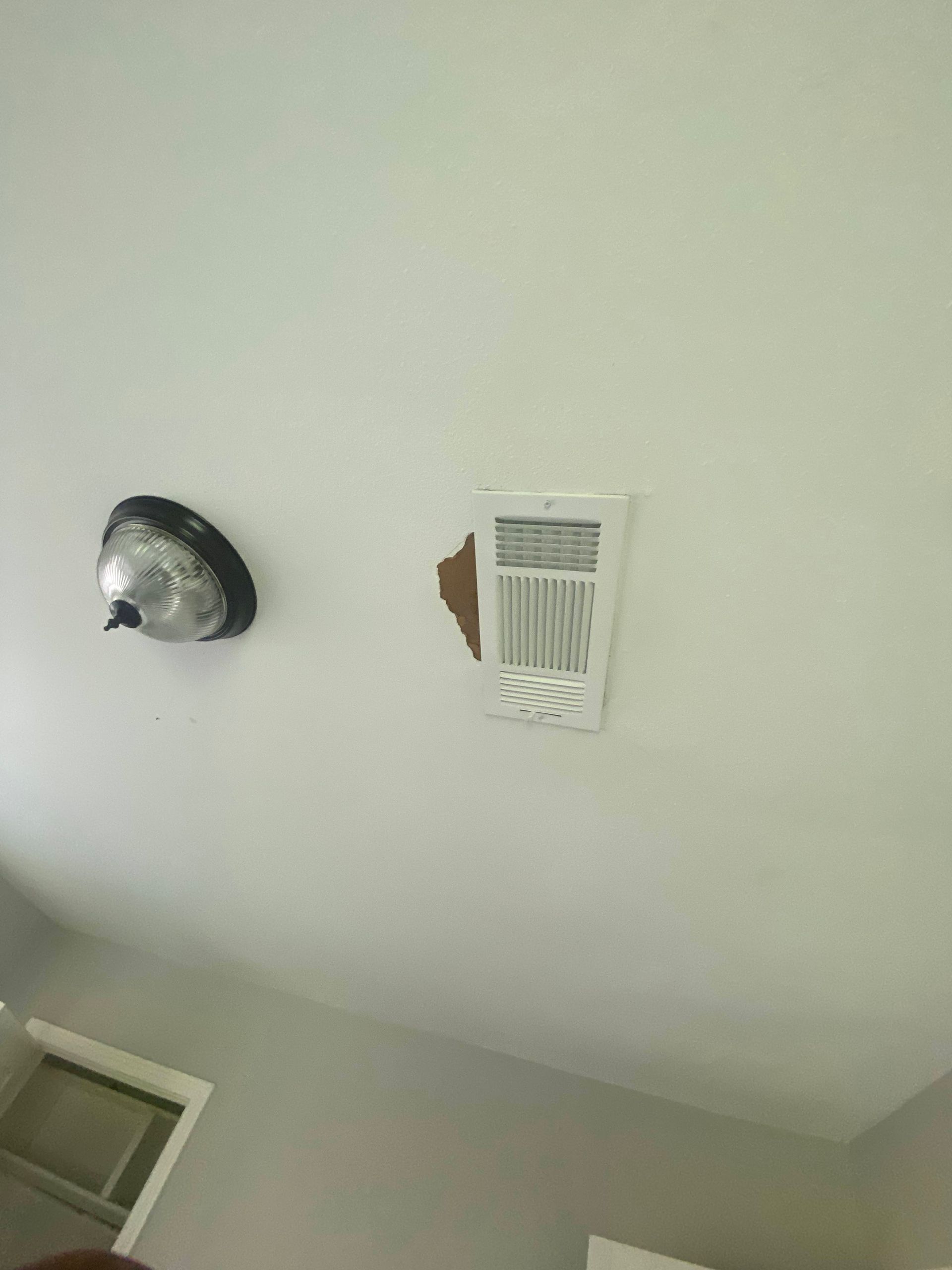 White ceiling with a silver light fixture and a damaged vent cover.