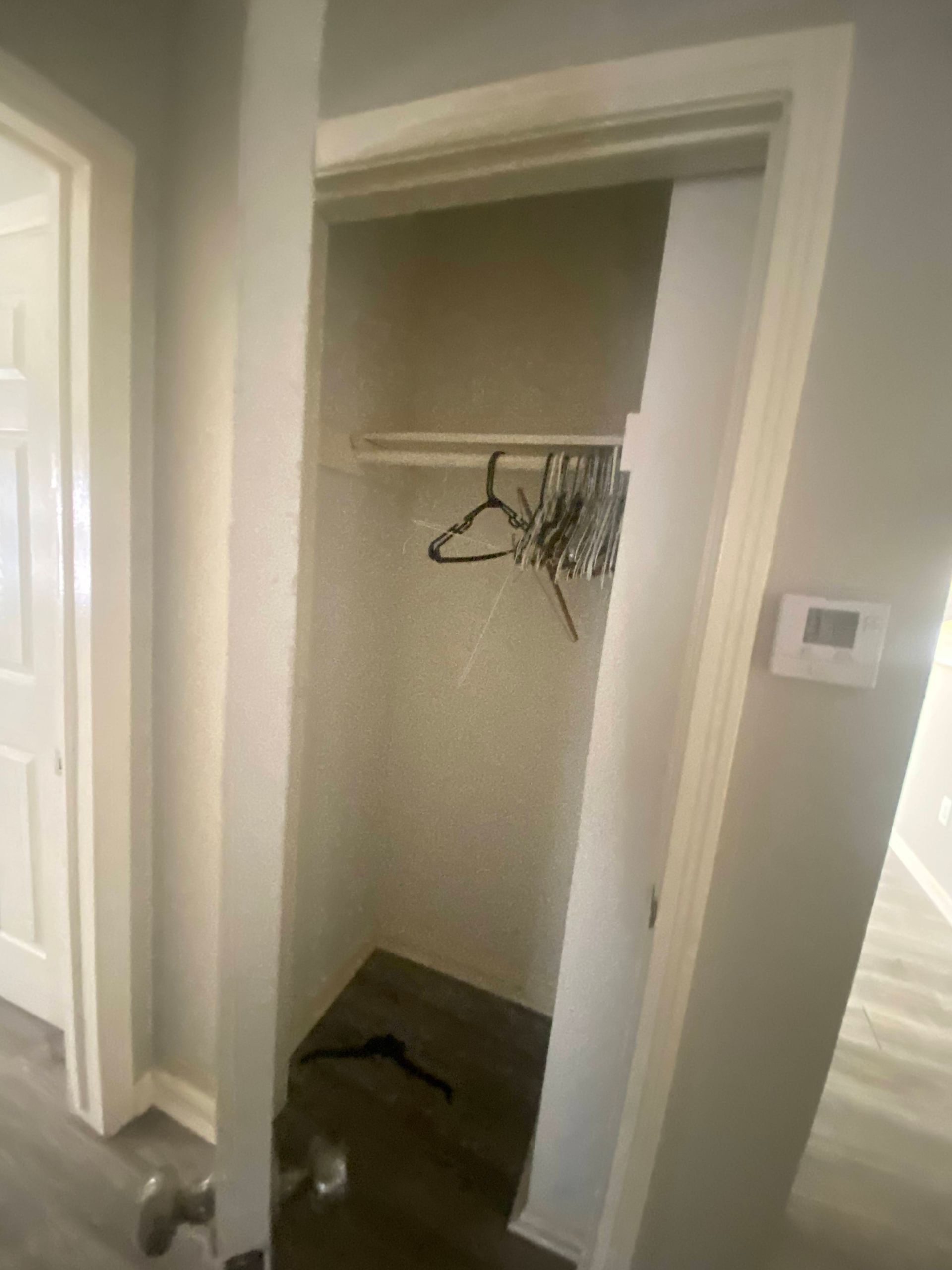 Open closet with clothes hangers inside; door ajar. Beige walls, wood-look floor.