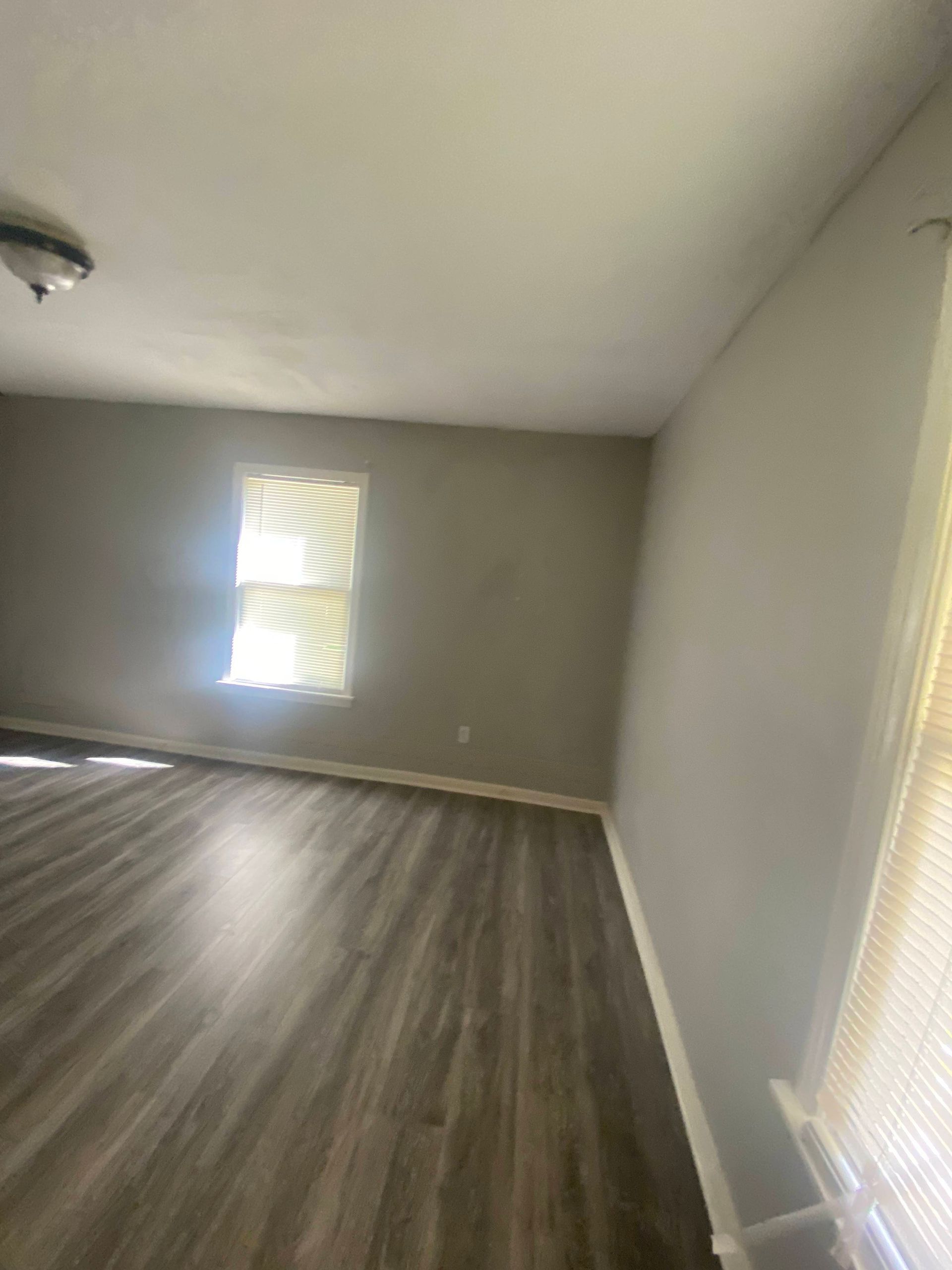 Empty room with gray walls, wood-look flooring, and a window with blinds.