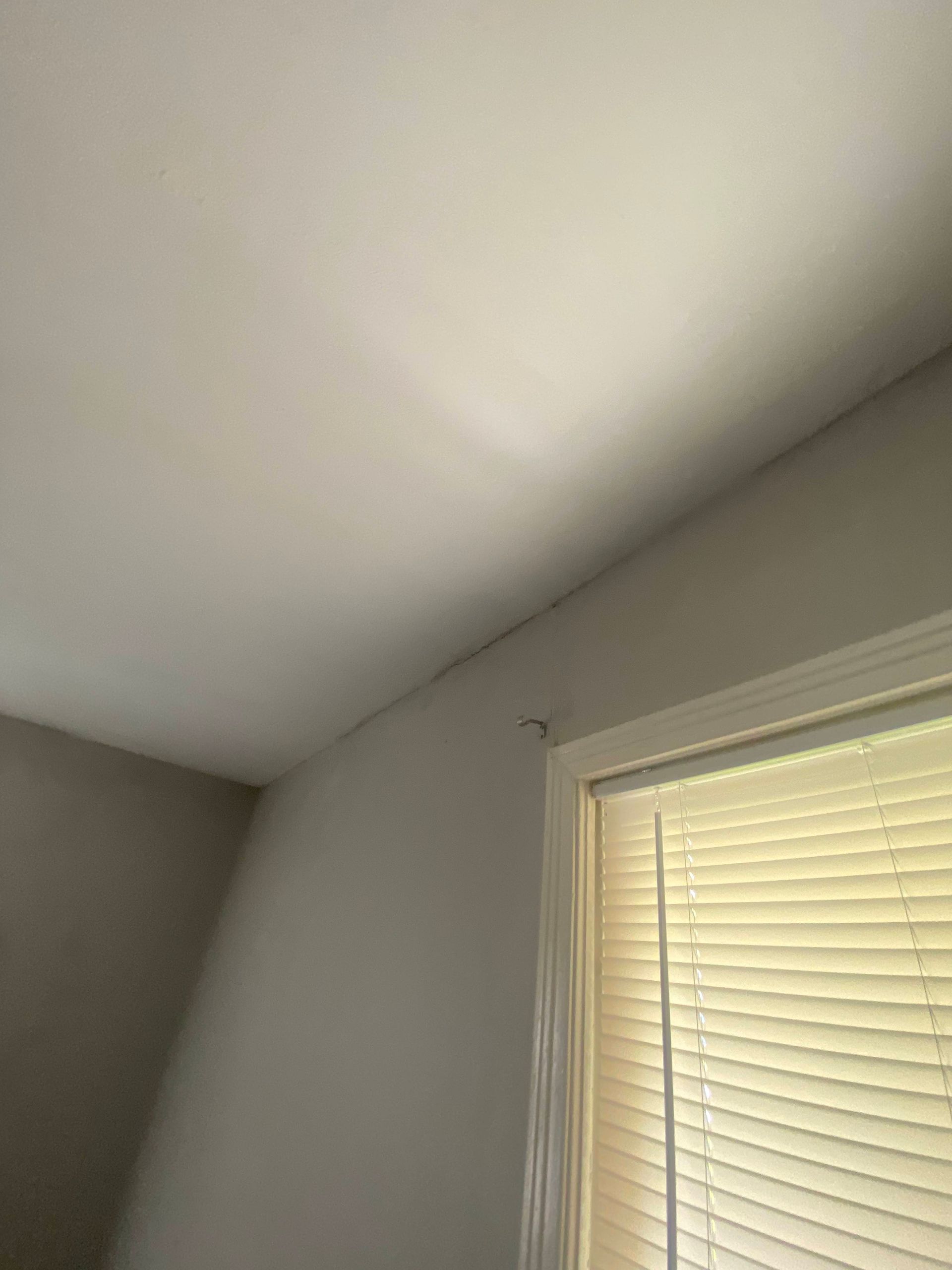 White ceiling meets a light gray wall near a window with closed blinds.