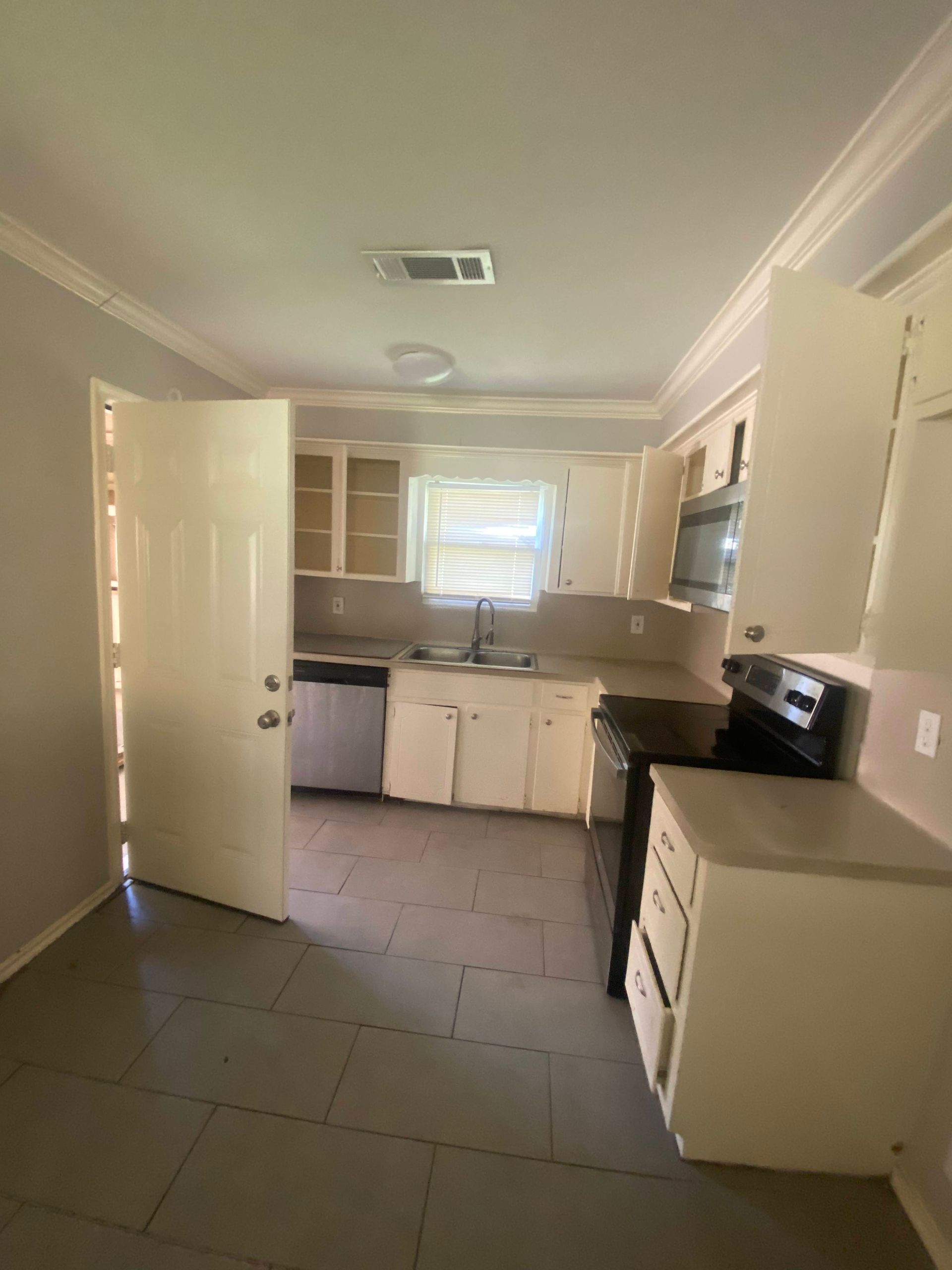 Kitchen with white cabinets, appliances, and tile floor; doorway on left.
