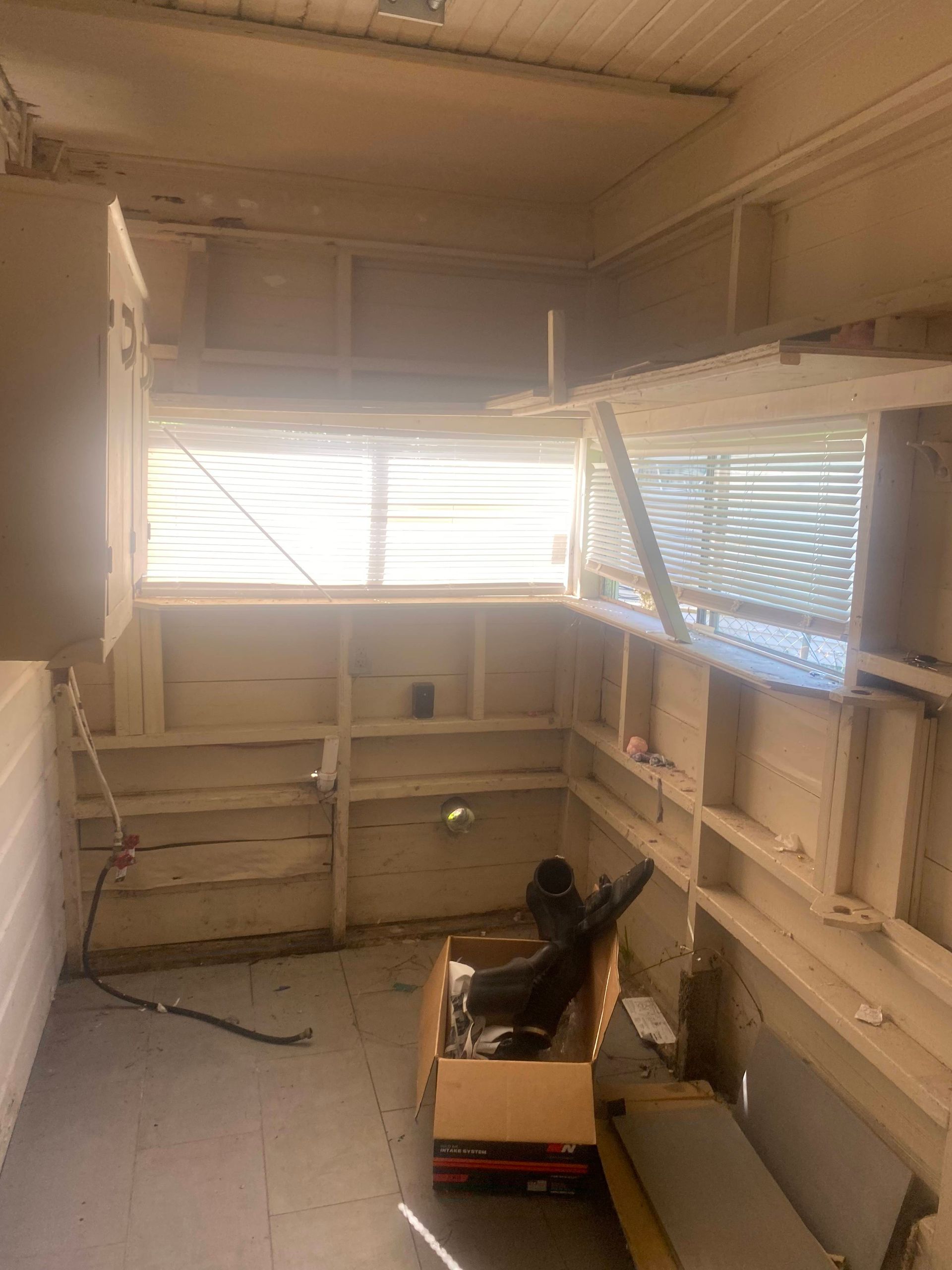 Empty room with built-in shelving and cabinets; bright light coming through the window blinds.
