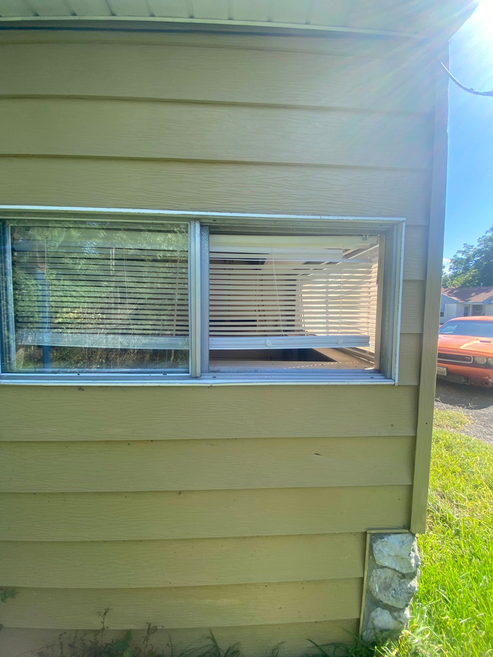 Window with blinds in a yellow building's side. Bright sunlight reflects on the glass.