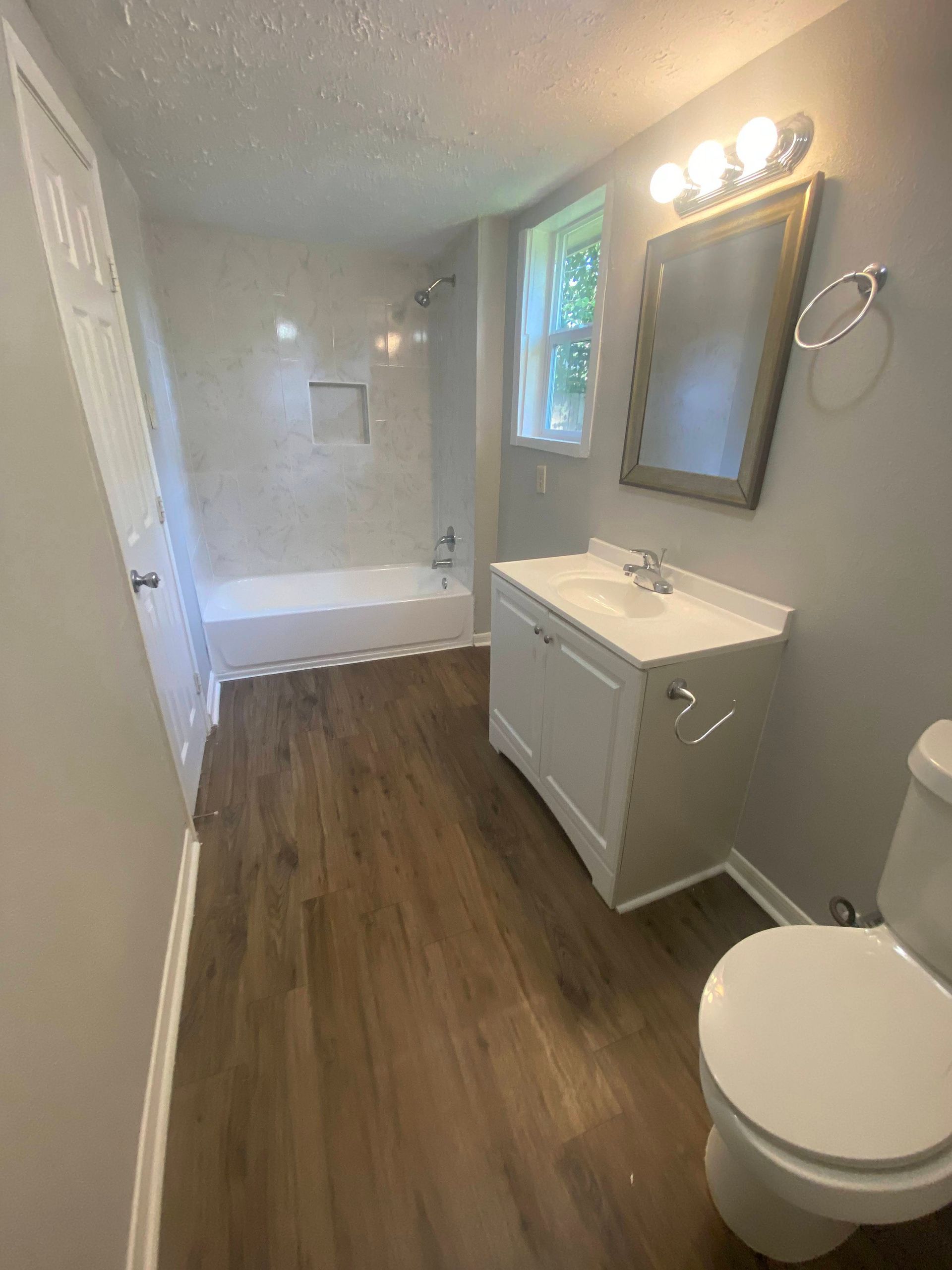 Bathroom with white vanity, toilet, and bathtub. Wooden floor, gray walls.