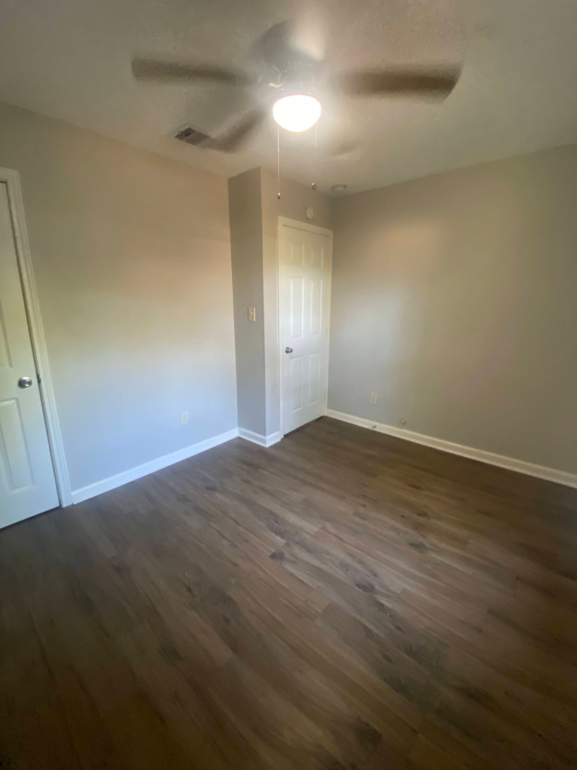 Empty room with wood-look flooring, light grey walls, white trim and ceiling fan. Two white doors visible.