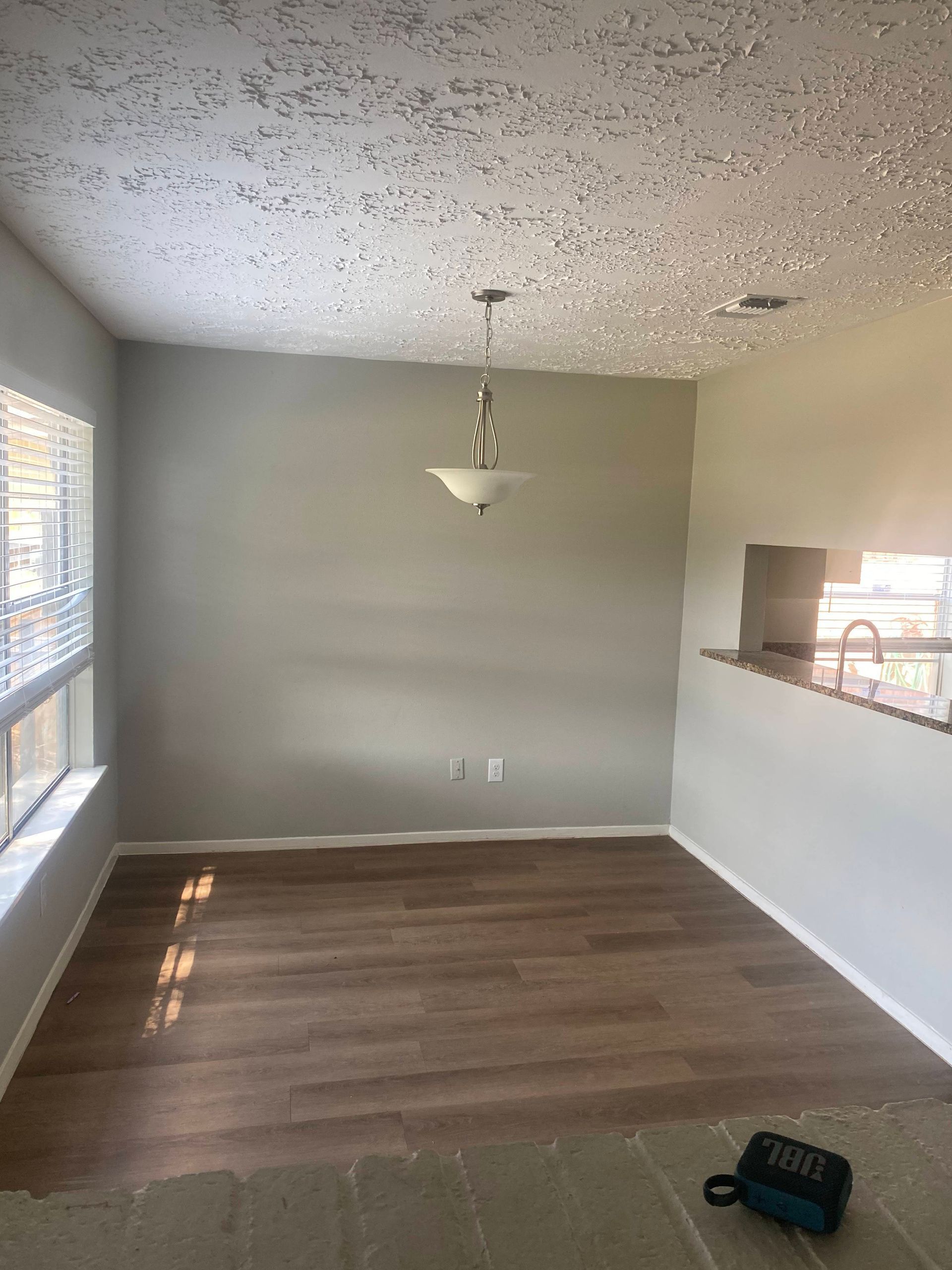 Empty dining room with gray walls, wood floors, and textured ceiling, lit by a hanging light fixture.