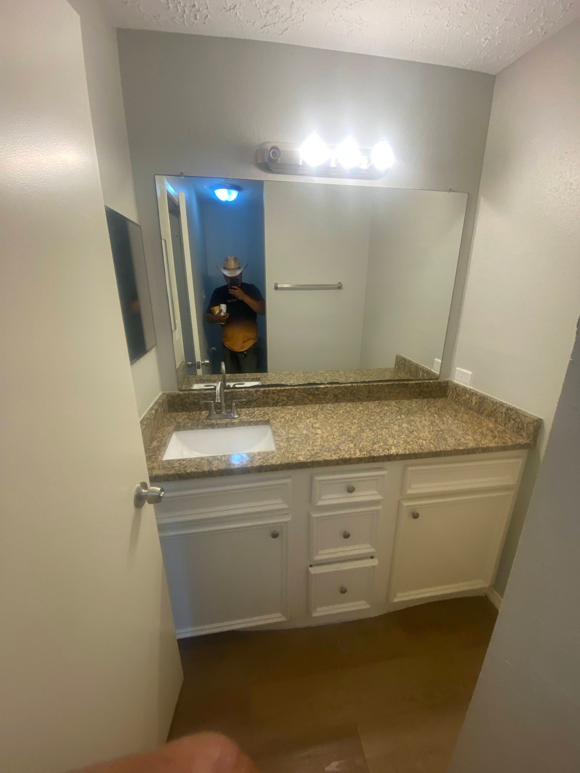 Bathroom with white vanity, granite countertop, large mirror, and person reflected in the mirror.