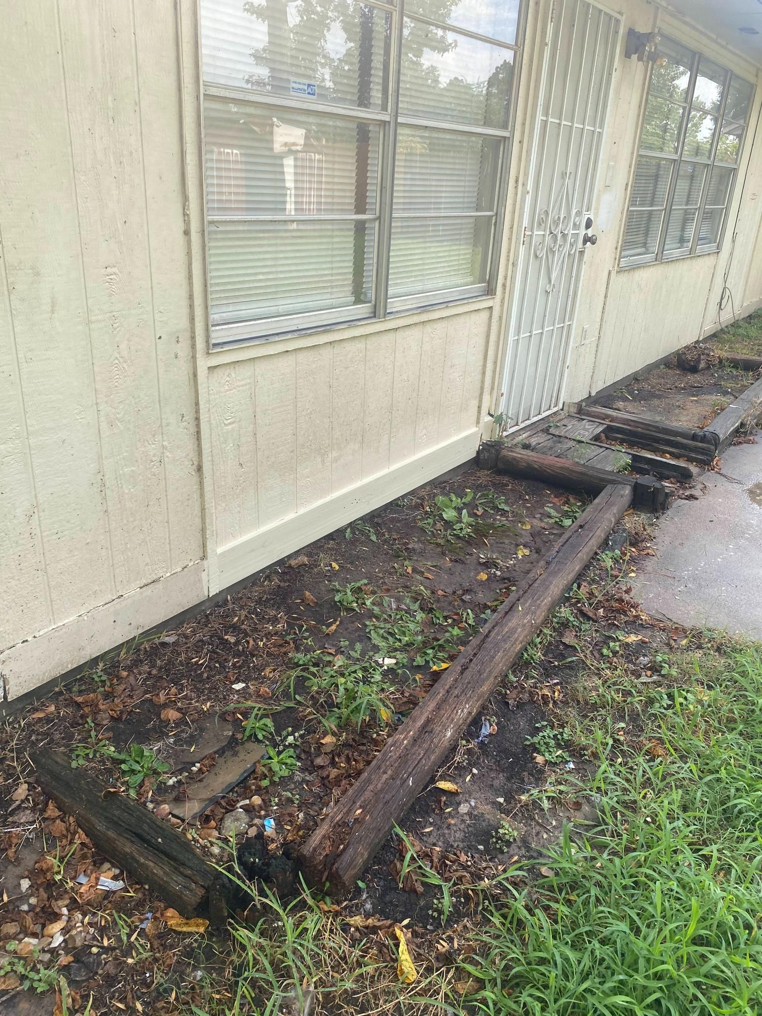 Exterior of a building with weathered wood boards along the wall and dirt, grass, and a window.
