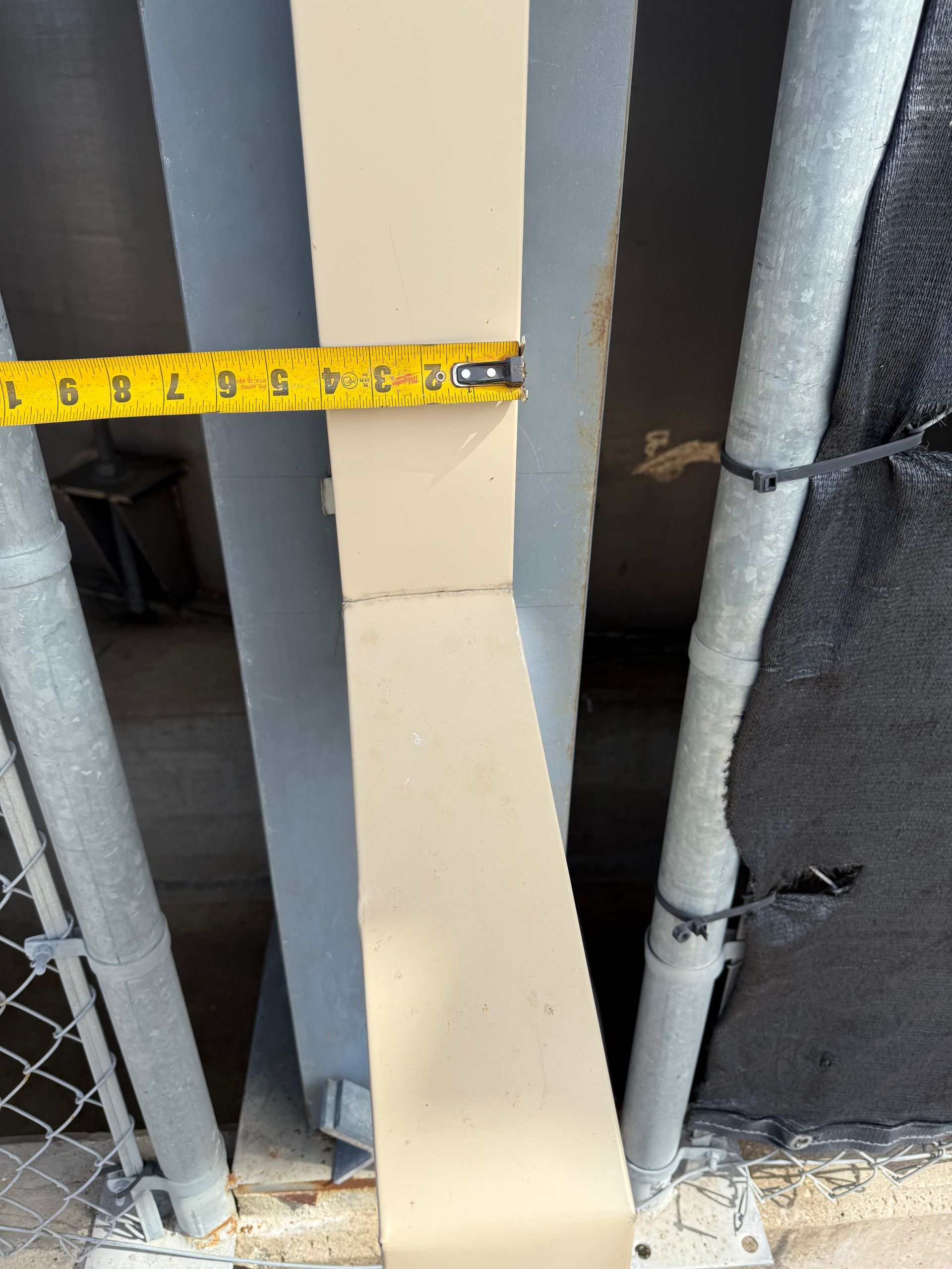 Yellow tape measure showing a 3-inch width on a beige metal beam.