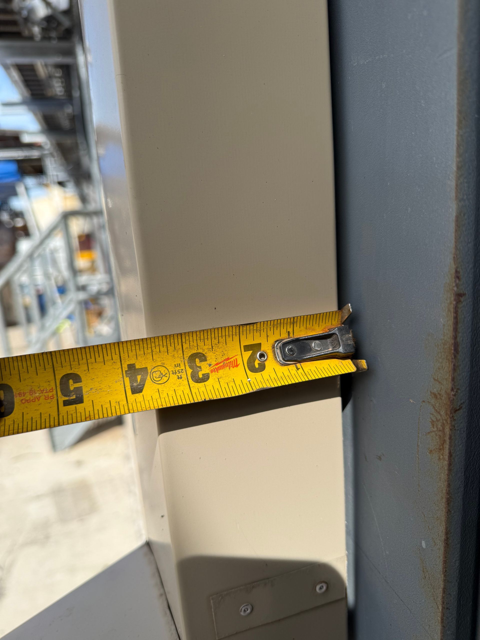A yellow tape measure showing 2 inches on a beige post, next to a gray metal support.