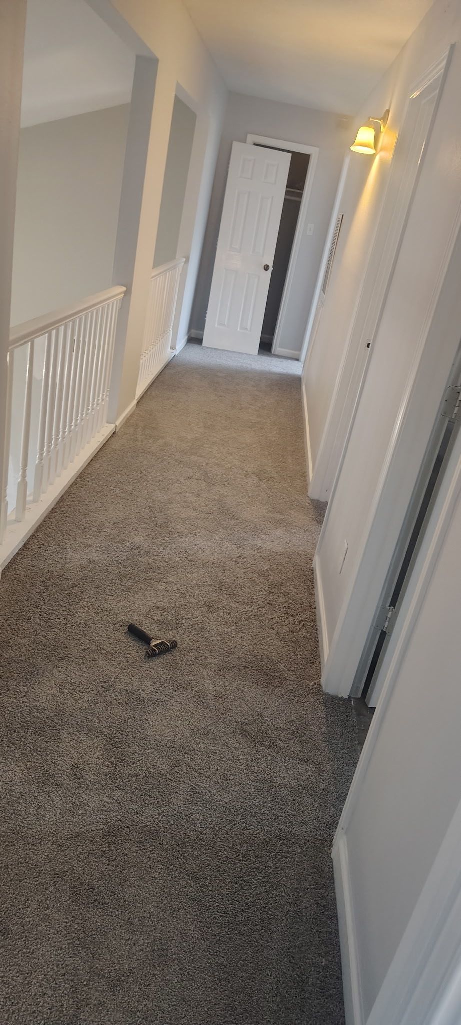 A hallway with light gray carpet and white doors on the right. A railing is on the left.