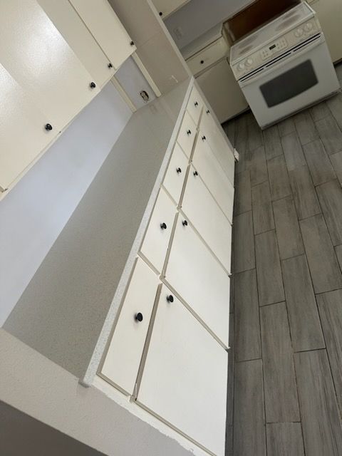 White kitchen cabinets and oven against gray wood-look floor.