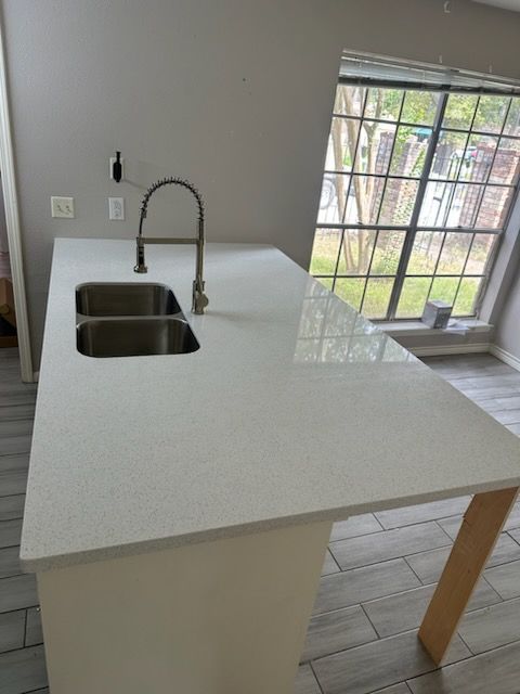 Kitchen island with white countertop, stainless steel sink, and faucet near a window.