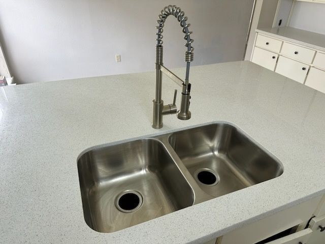 Stainless steel double kitchen sink with tall faucet on a white countertop.