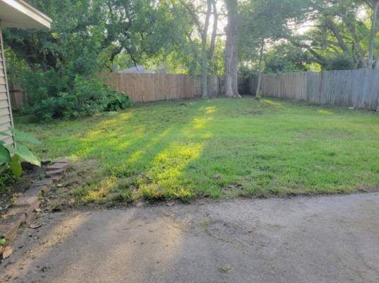 Backyard with grassy lawn, wooden fence, and concrete patio in sunlight.