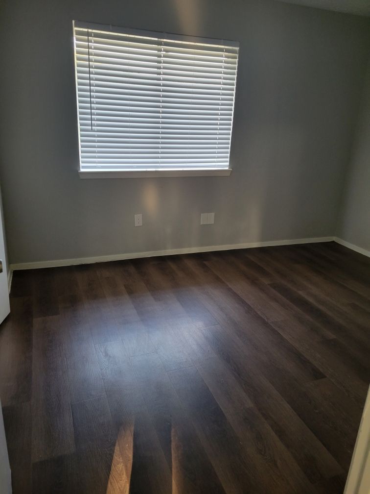 Empty room with wood floors, gray walls, and a window with blinds.