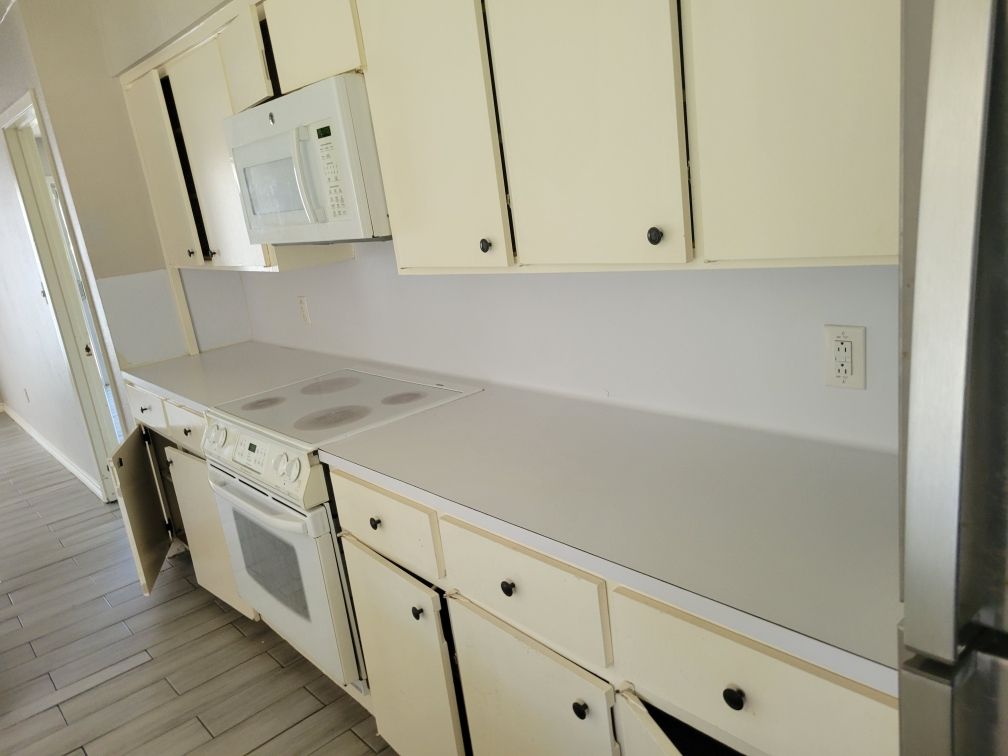 Off-white kitchen cabinets with a stove, microwave, and countertop against a light wall.