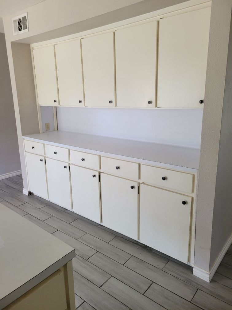 White built-in cabinetry with several doors and drawers in a room with light wood-look flooring.