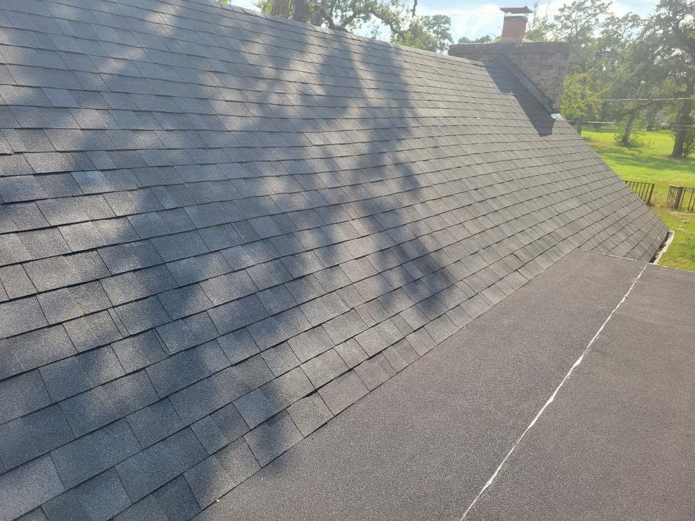 Dark asphalt shingles on a roof, shadows cast across them.
