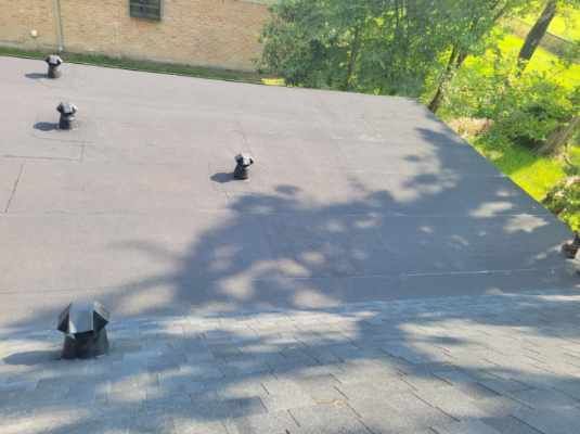 Black flat roof with several vents, sunlight casting shadows.
