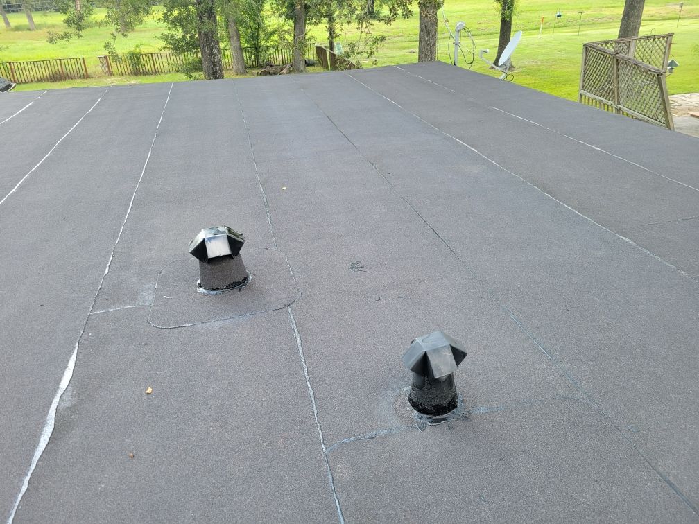 Black flat roof with two vent pipes and green surroundings.