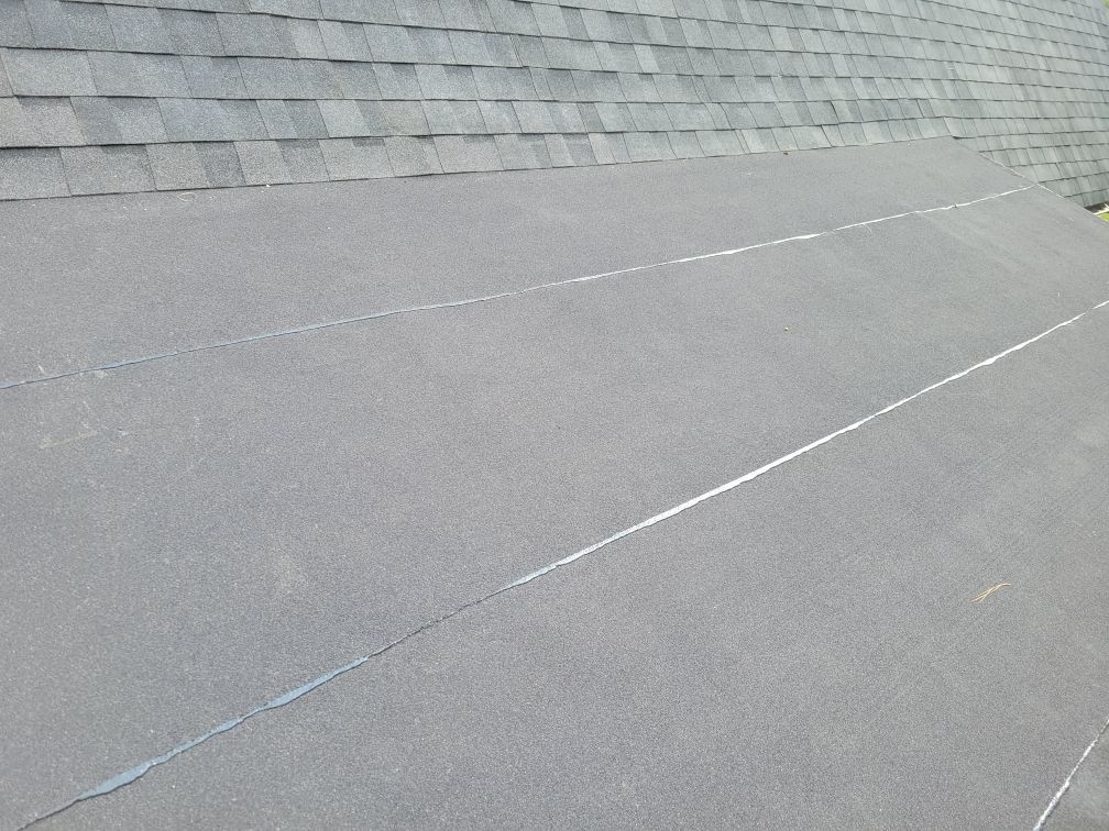 Dark gray flat roof with seams, next to gray shingled roof section.