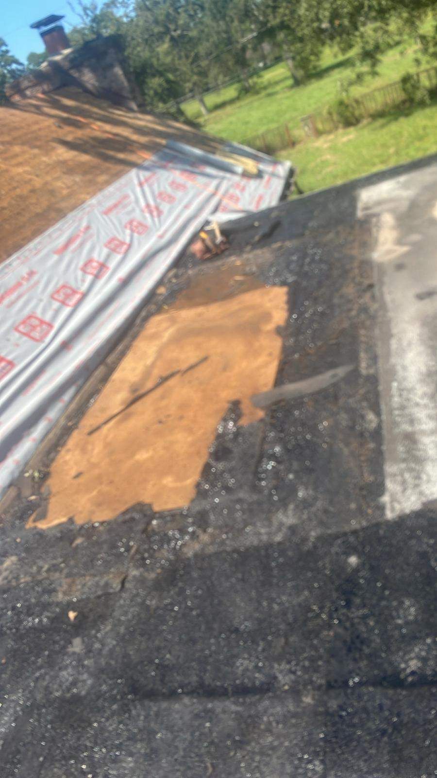 Damaged flat roof with exposed wood and new underlayment partially installed.
