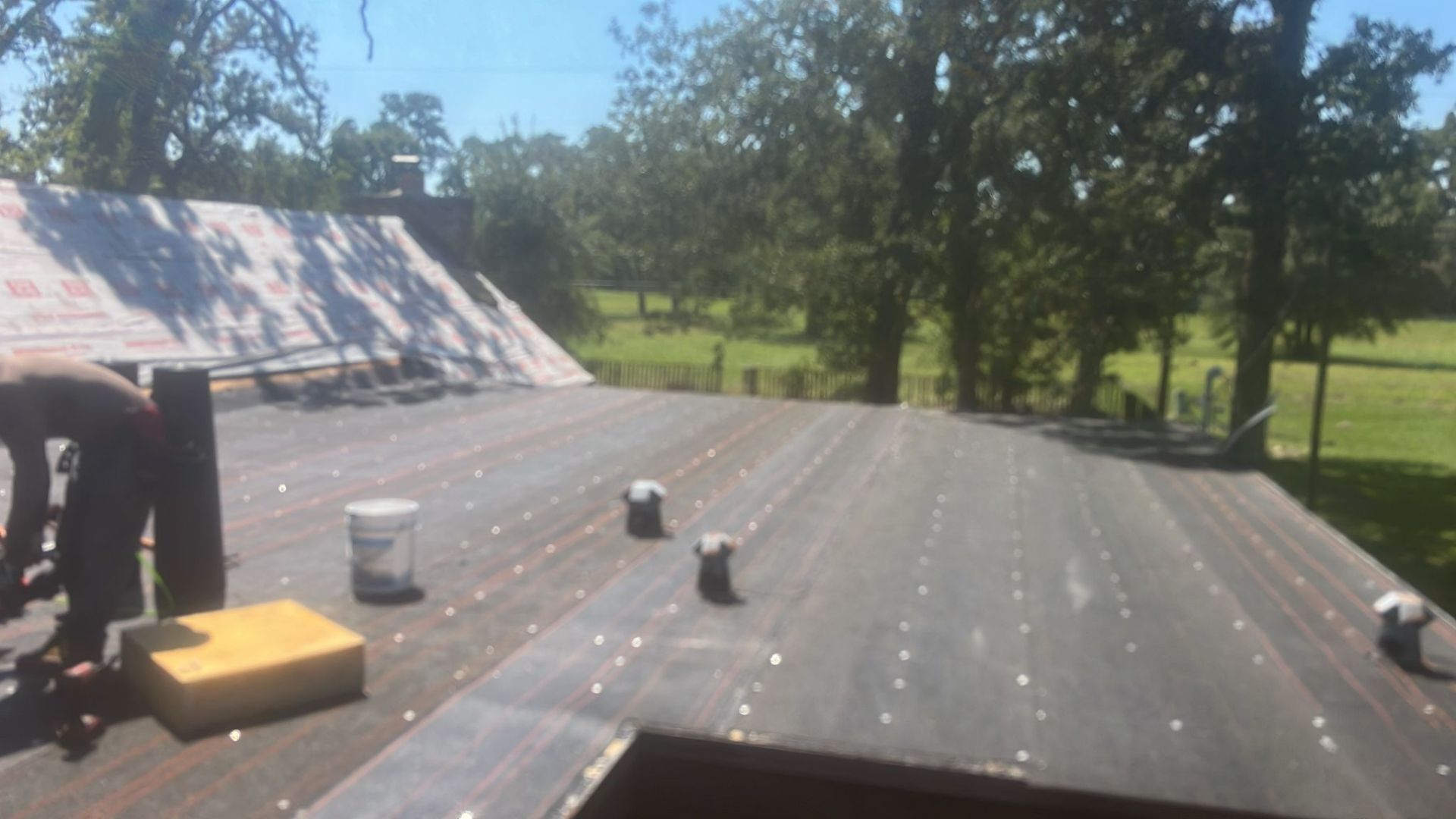 Roof being worked on; person in the frame, rolls of material, sunny day.