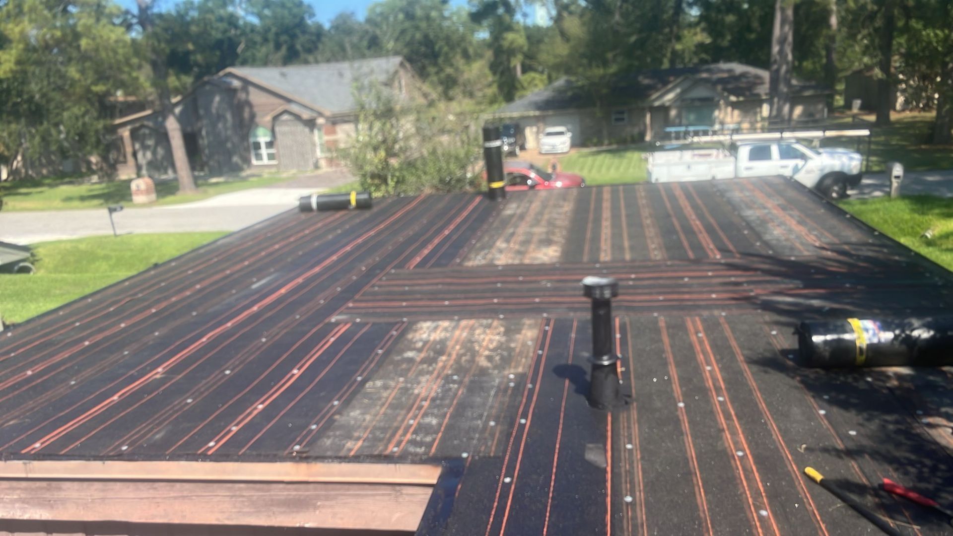 Black roof with orange heating elements, two chimneys, and nearby houses.
