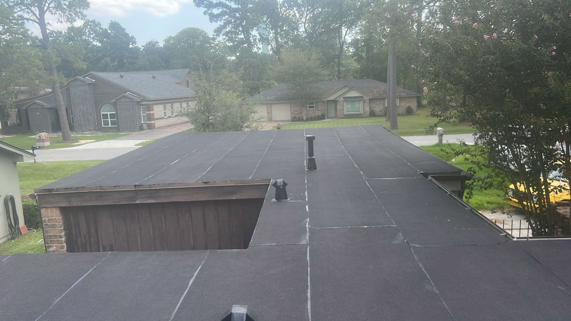 Black flat roof with vents, overlooking a neighborhood with green trees and houses.
